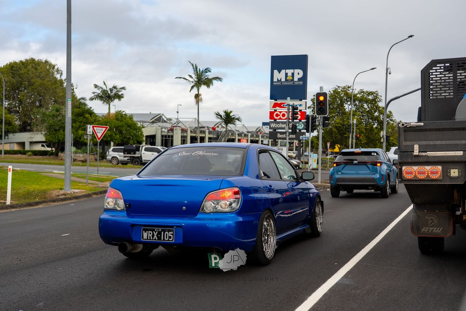 A blue sports car parked on a winding road surrounded by palm trees and greenery.