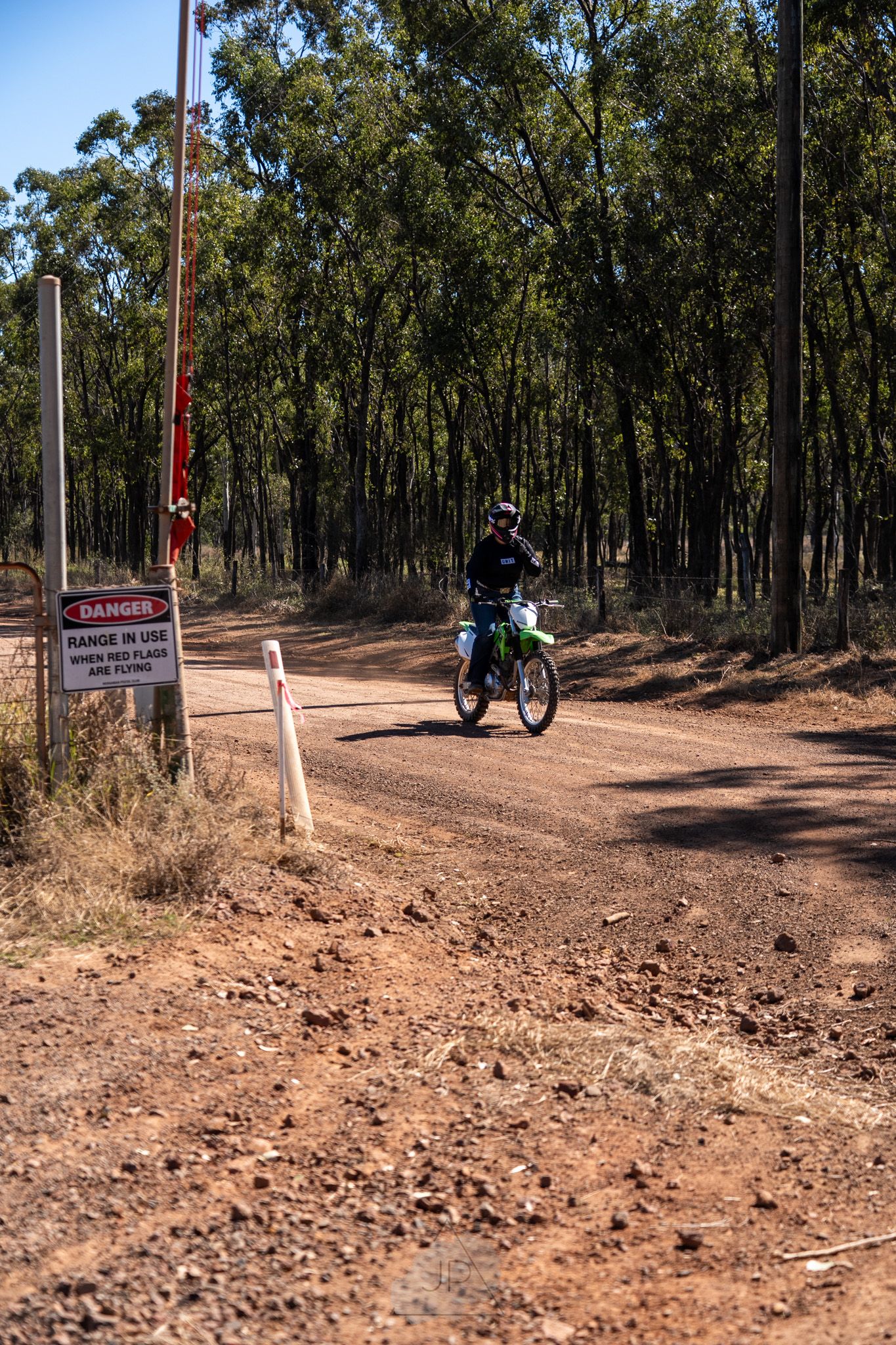A dirt bike rider navigates a forest trail past a danger sign with eucalyptus trees in the background.