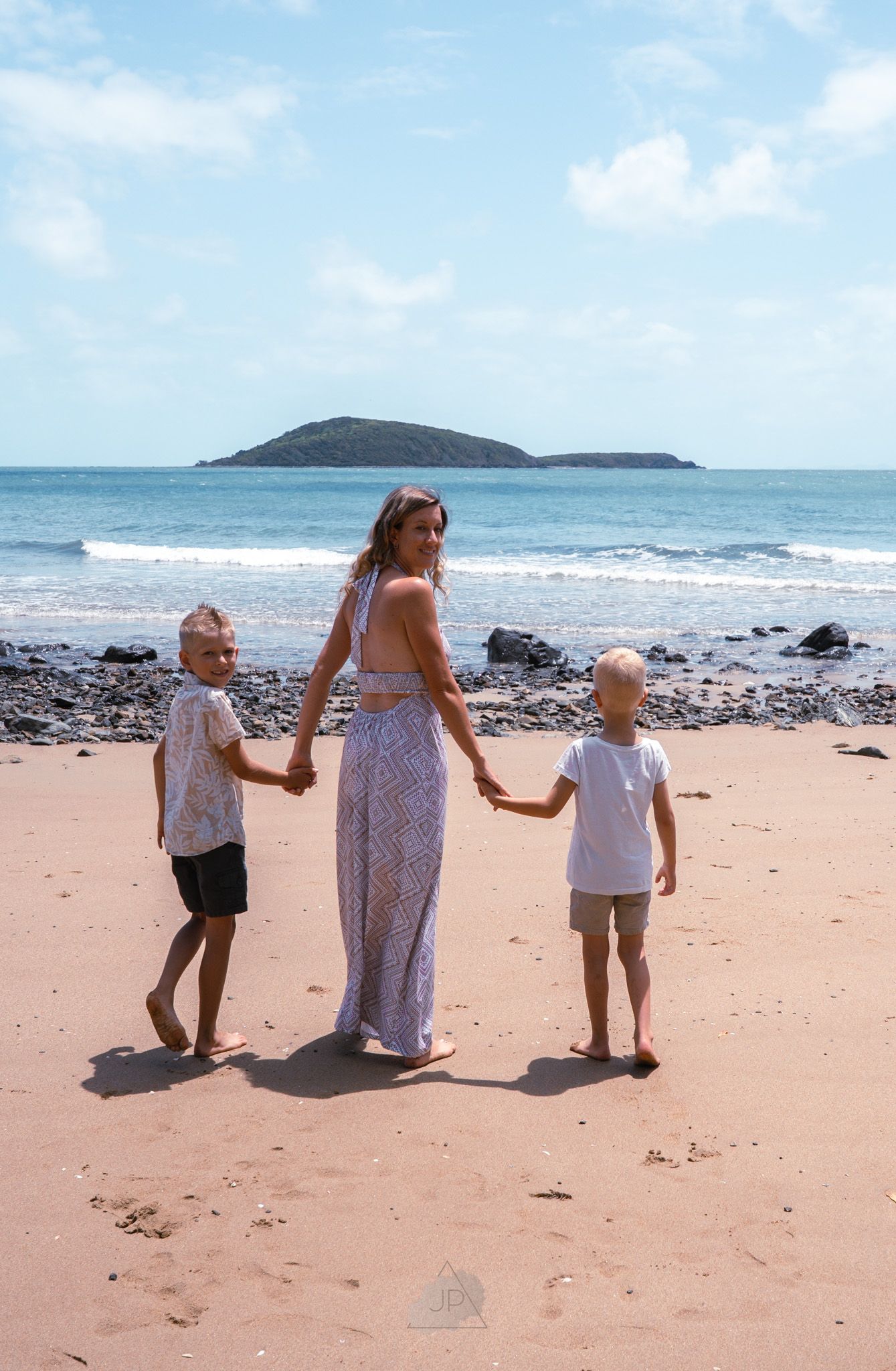 Family walking together along a scenic beach with rocky shore and island views in the background.