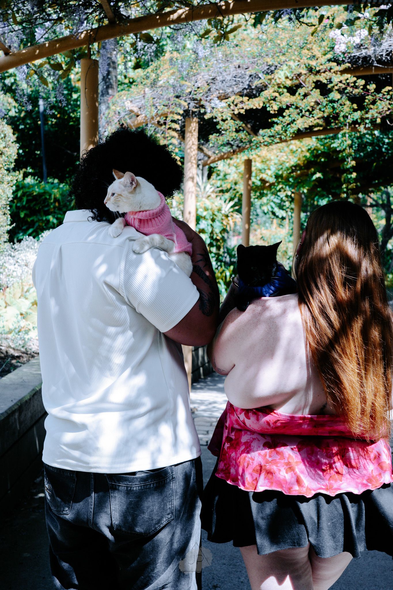 Two people in white and pink outfits dance together in a shaded outdoor setting.