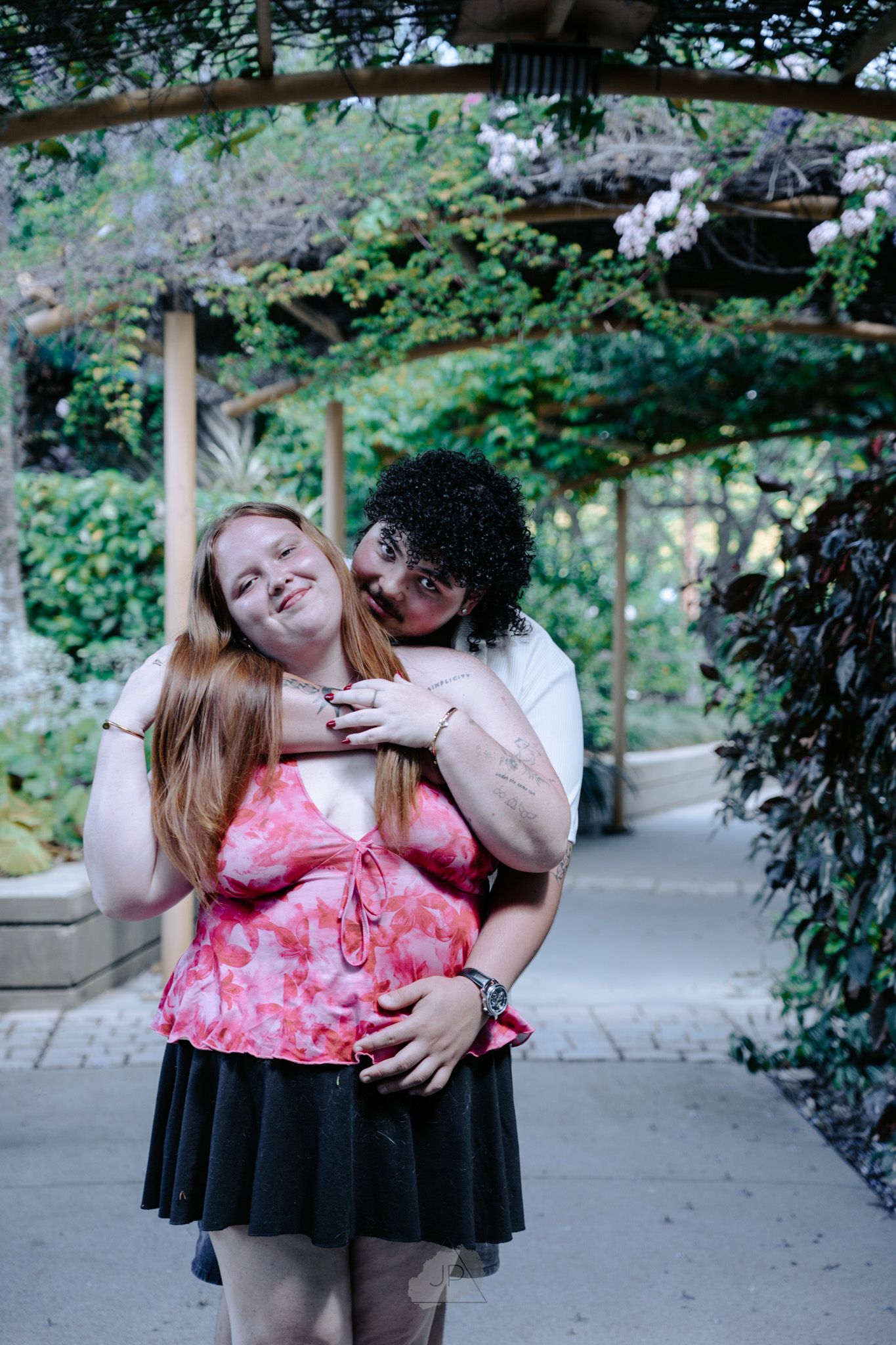 A couple shares tender moments together in a garden walkway wearing pink and black outfits.