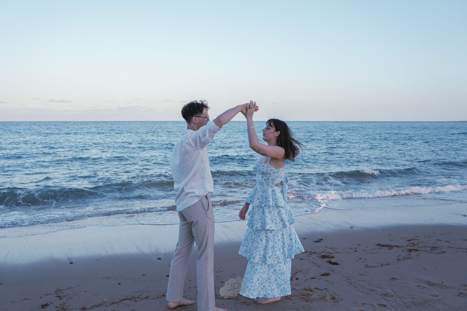 Romantic couple dancing together on a serene beach at sunset with ocean waves in the background.