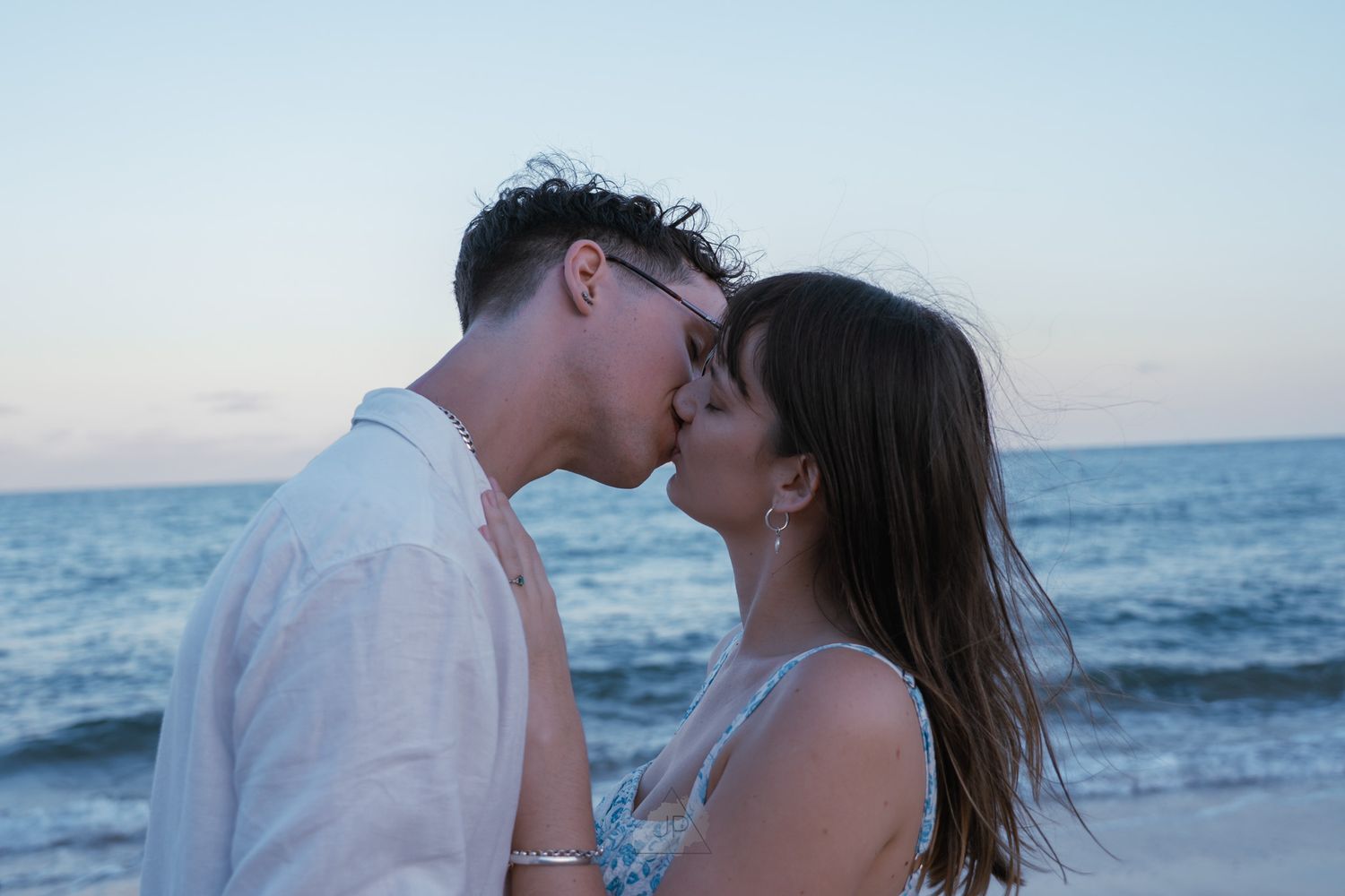 Romantic couple sharing intimate moments on a beach at sunset with ocean waves in the background.