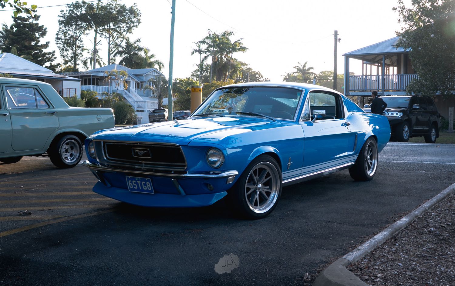Row of classic Ford Mustangs in various shades of blue parked along a street at sunset.