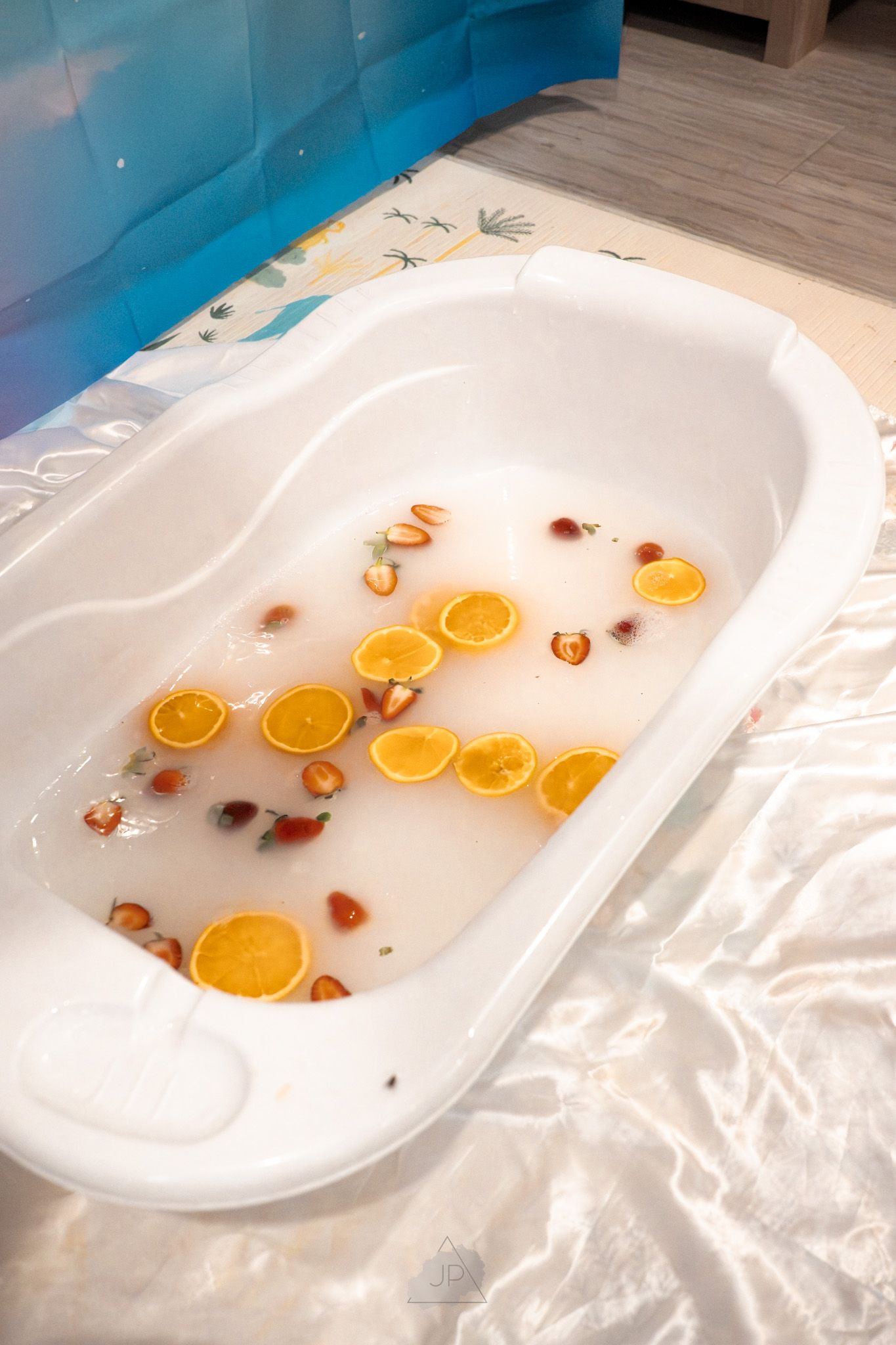 A white bathtub filled with water contains floating orange citrus slices and dried flowers creating a relaxing bath scene.