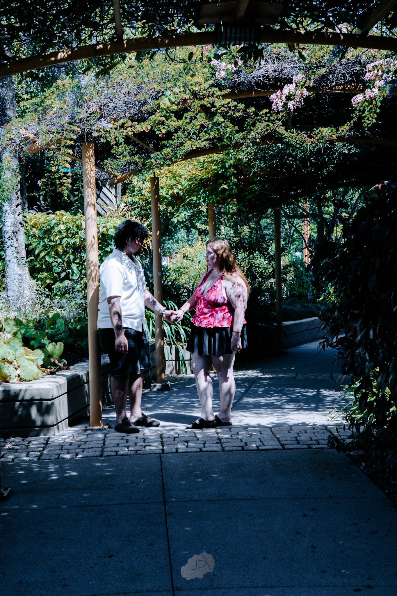 People enjoying a shaded walkway in a lush garden setting on a sunny afternoon.