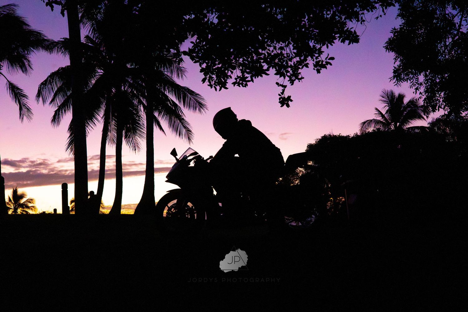 Palm trees silhouetted against a vibrant purple and pink sunset sky create a tranquil tropical scene.