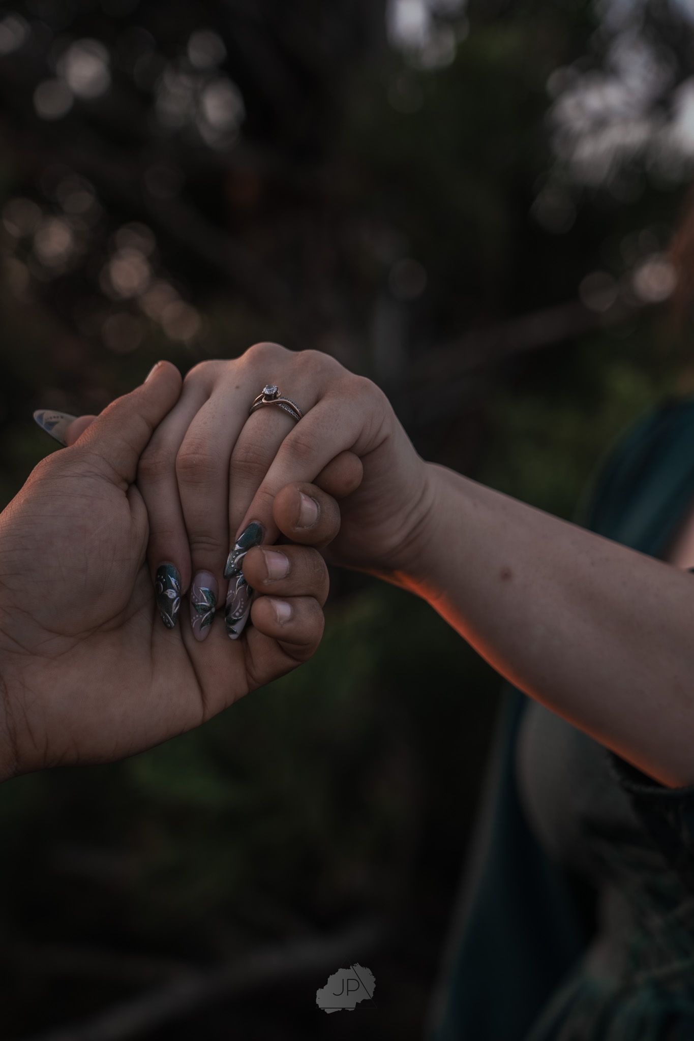 Two hands wearing engagement rings reach out to touch each other in a romantic gesture against a dark background.
