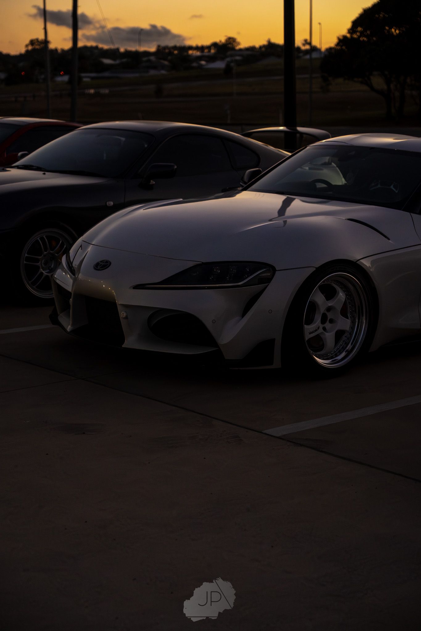 A white Toyota Supra sports car parked at sunset, showcasing its sleek silhouette and modified stance.