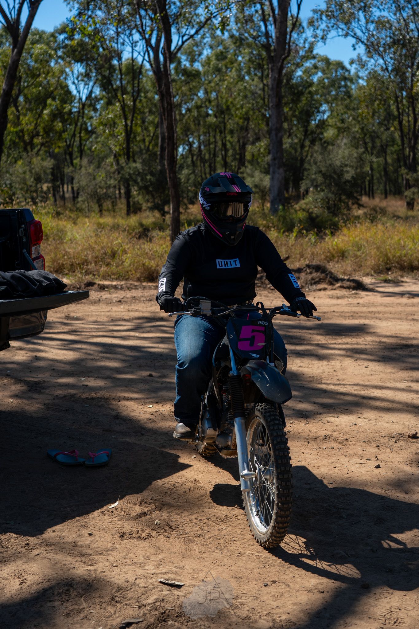Dirt bike rider in protective gear navigating a forest trail on a sunny afternoon.