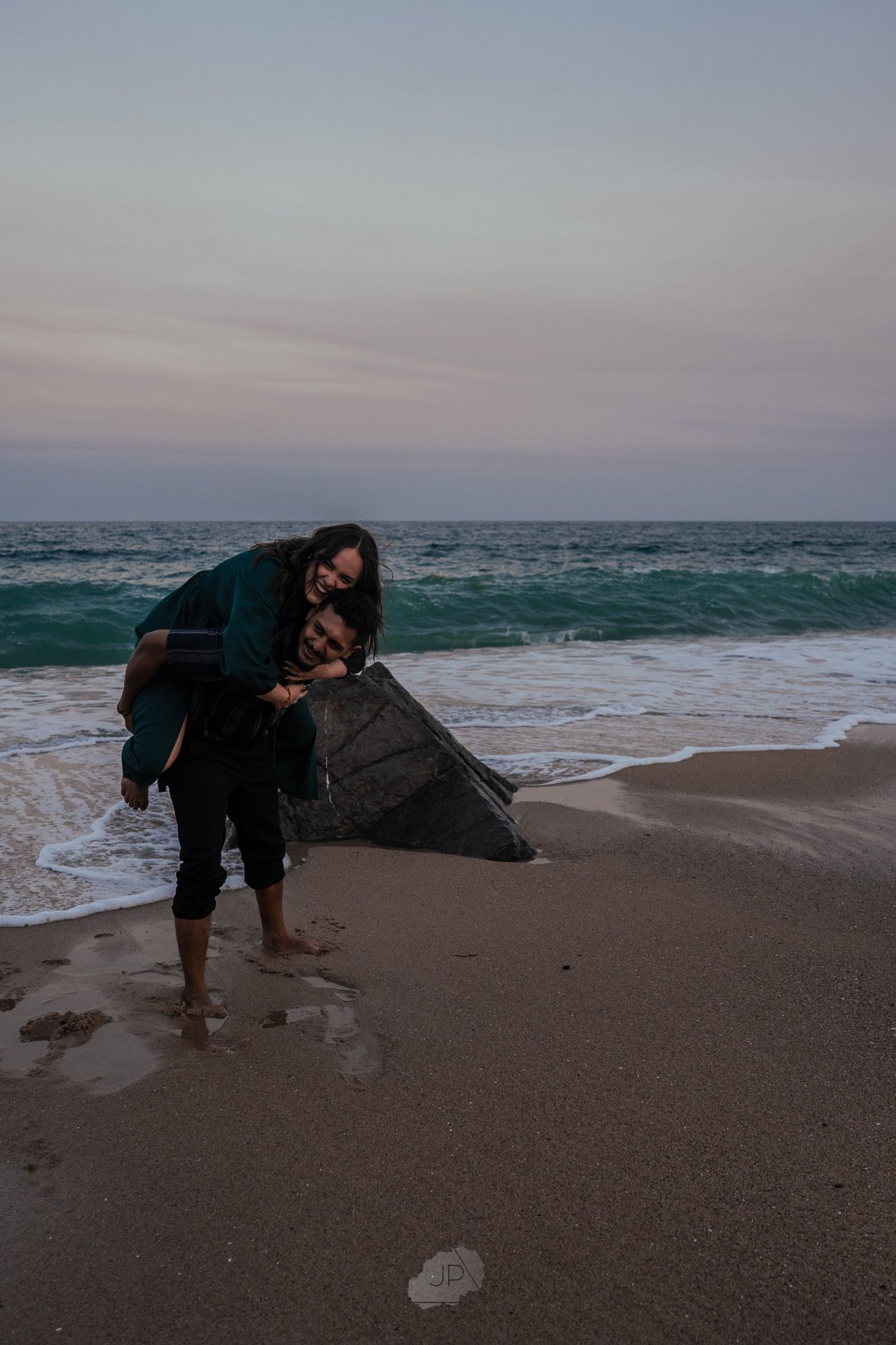 People bending down to examine something on a misty beach at sunset with waves crashing in the background.