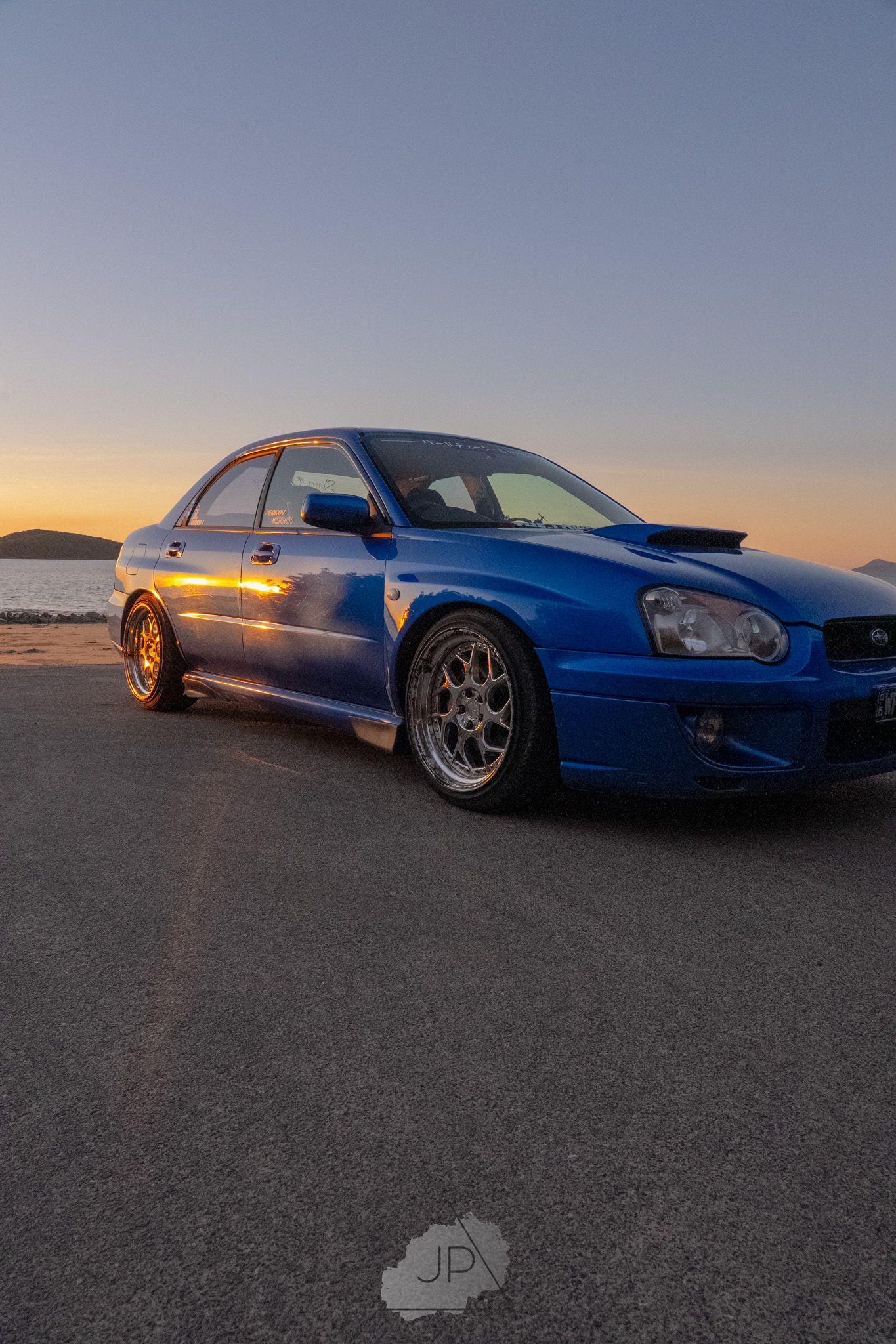 Blue Subaru WRX STI photographed at sunset against an empty desert landscape with dramatic side lighting.