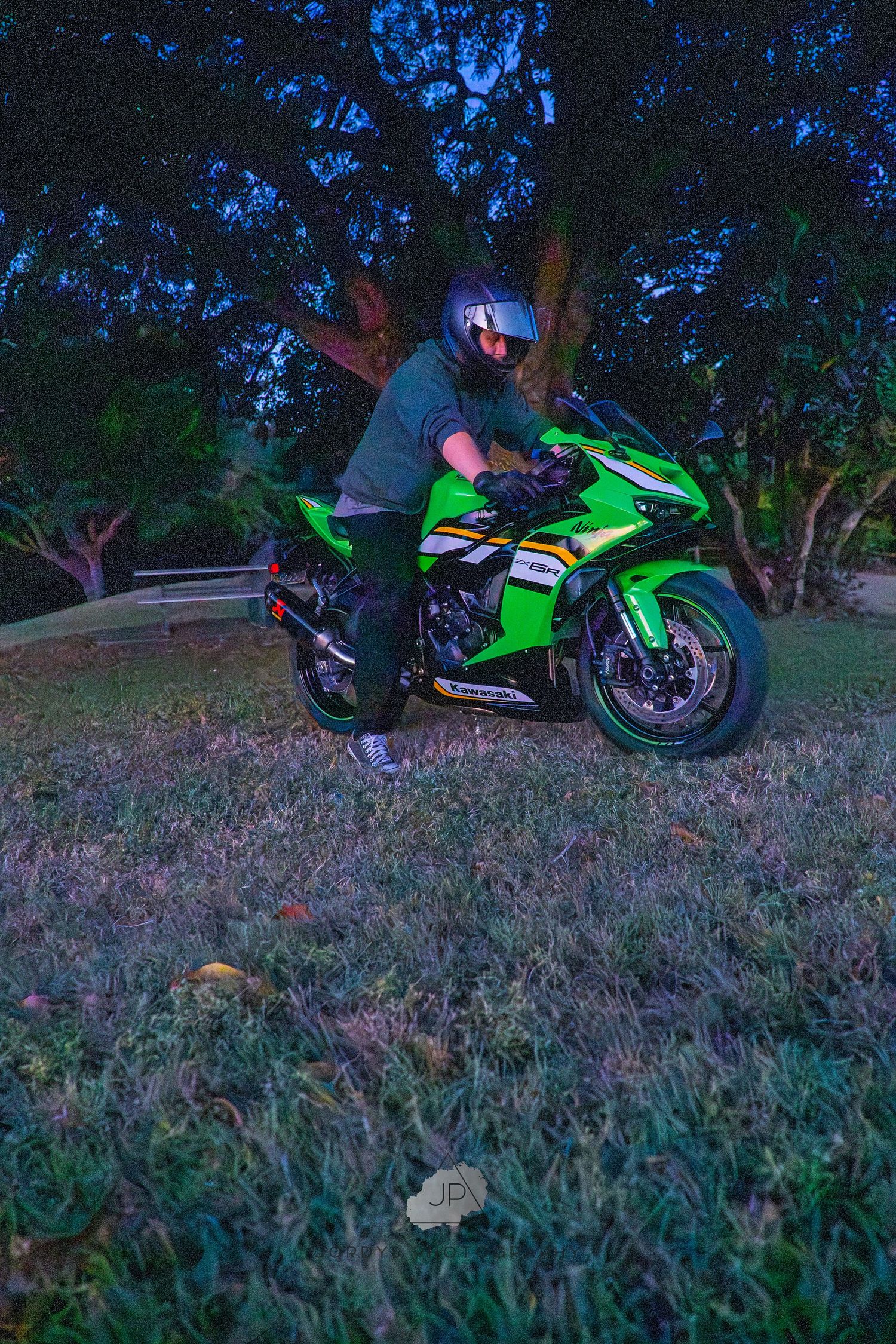 A bright green sport motorcycle parked on grass at dusk with a dark blue sky in the background.