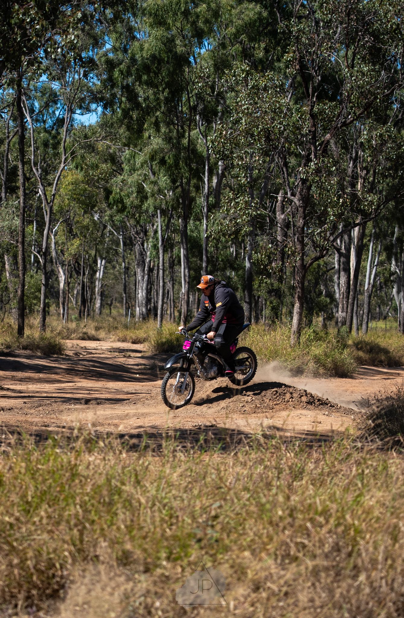 Mountain biker riding down a dirt trail through scenic eucalyptus forest on a sunny day in Australia.