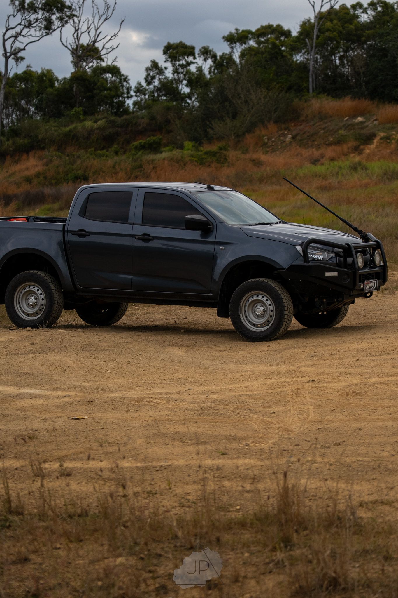 A black extended cab pickup truck parked on a dirt hill against a cloudy sky background.