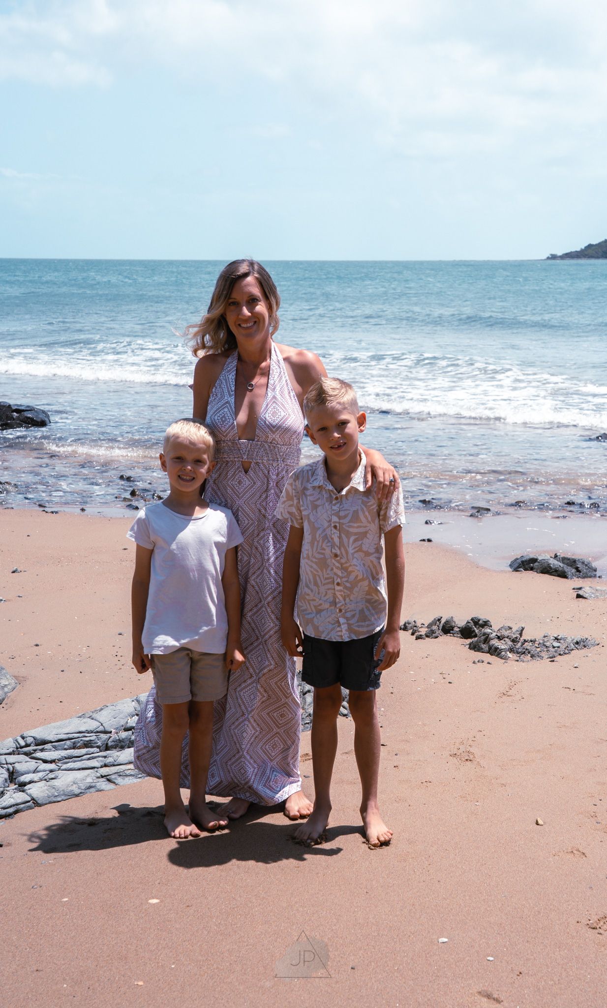 A beachside family portrait showing three people posing together on a sandy shore with ocean waves in the background.