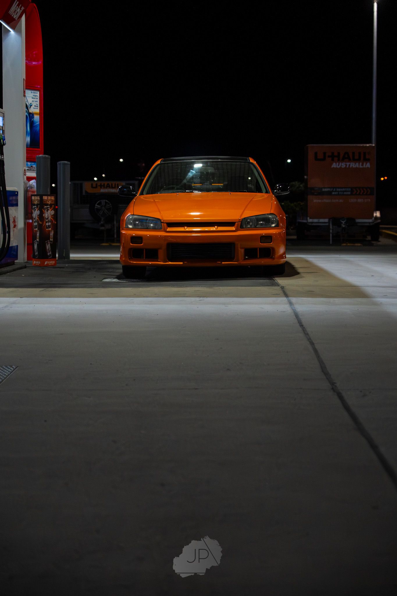 An orange Lamborghini sports car parked in a dimly lit garage with dramatic lighting.