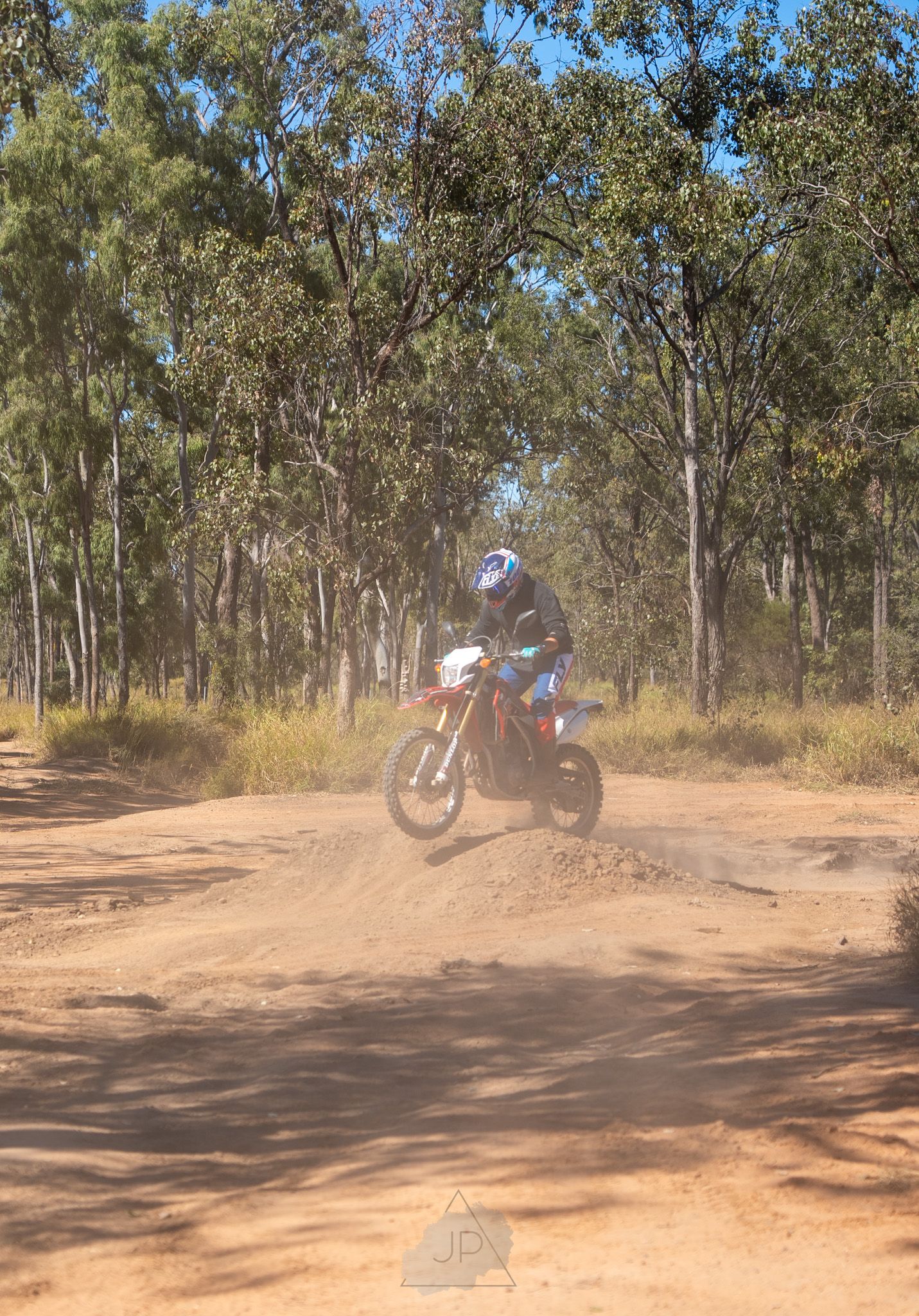Sequence of dirt bike performing a drifting turn on dusty trail through eucalyptus forest.