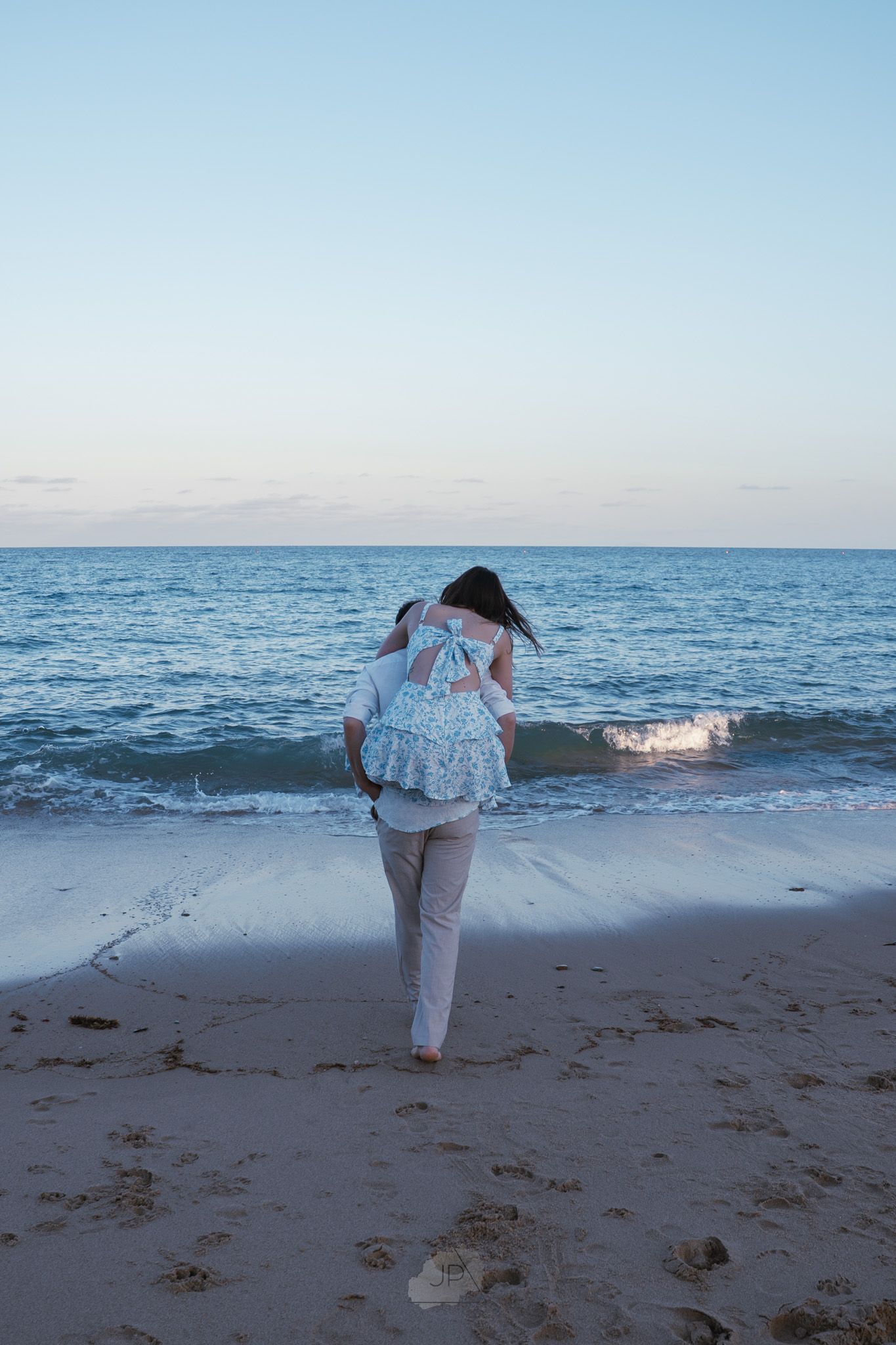 A person in white clothing performs a cartwheel sequence on a sandy beach at sunset with the ocean in the background.