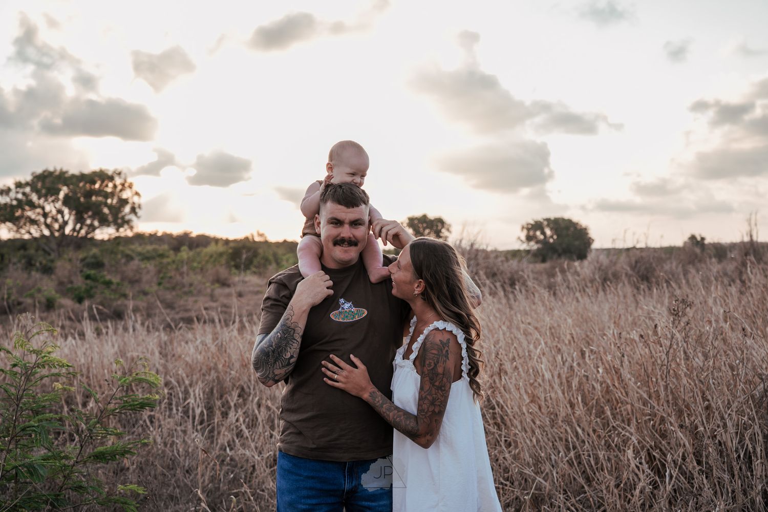 A family shares a tender moment together in a golden field at sunset with tall grass surrounding them.