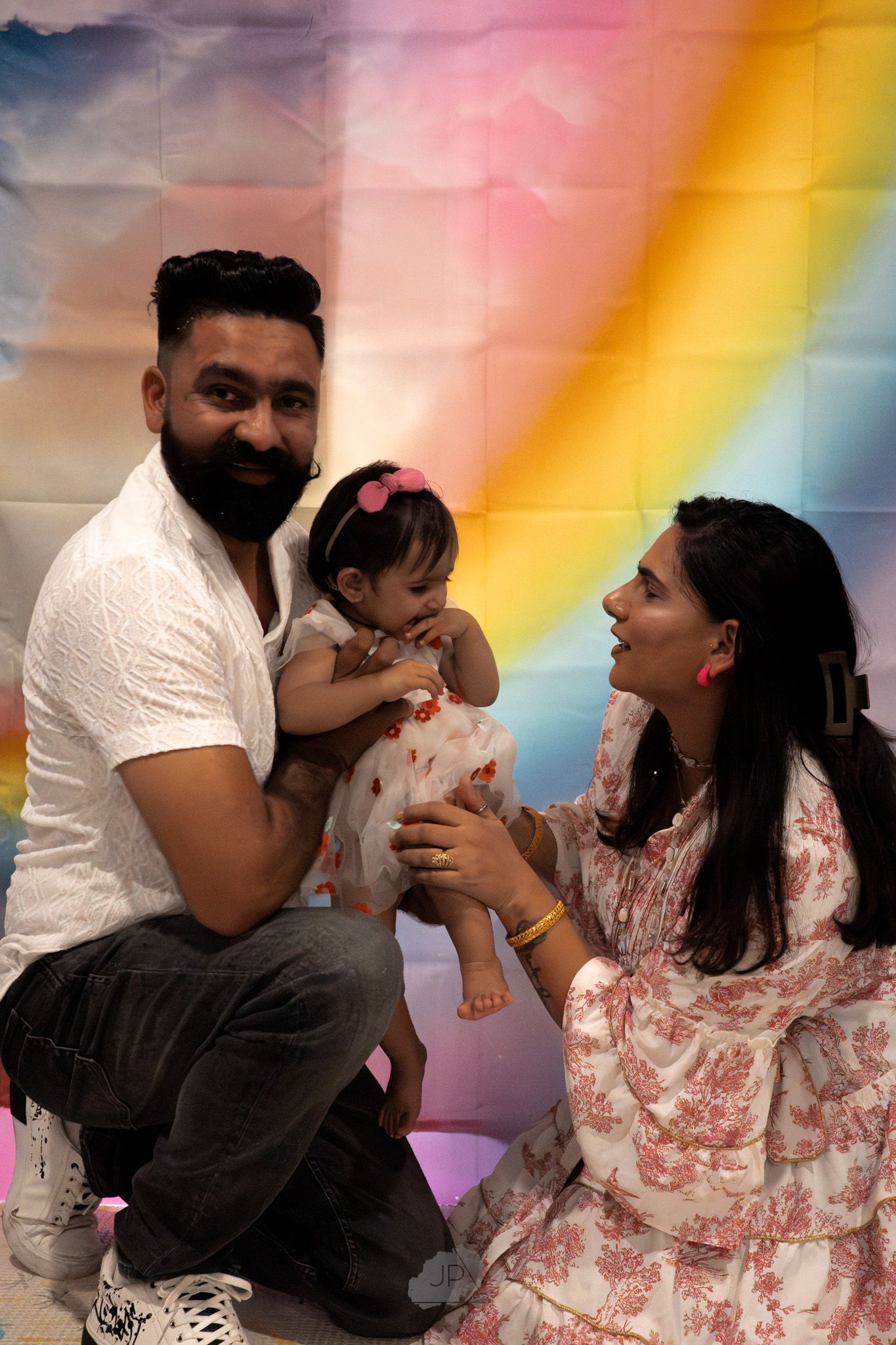 A family poses together against a colorful rainbow backdrop during a photo session.