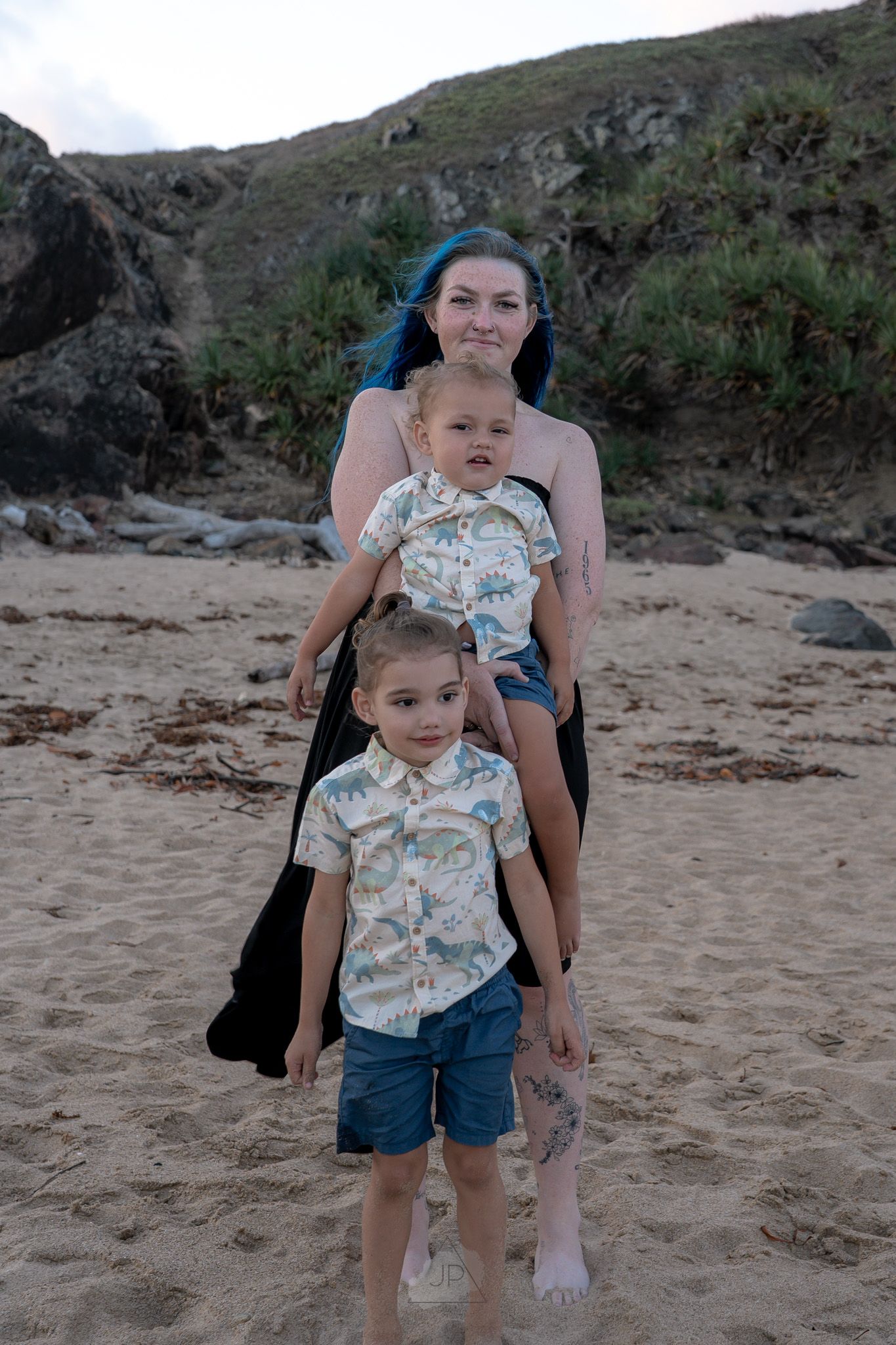 Candid family moments captured on a scenic beach with dramatic coastal cliffs and natural terrain in the background.