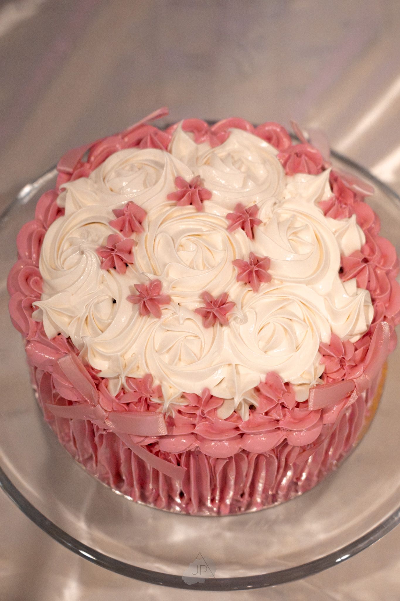Pink and white rosette decorated cake with swirled frosting patterns on a clear glass cake stand.