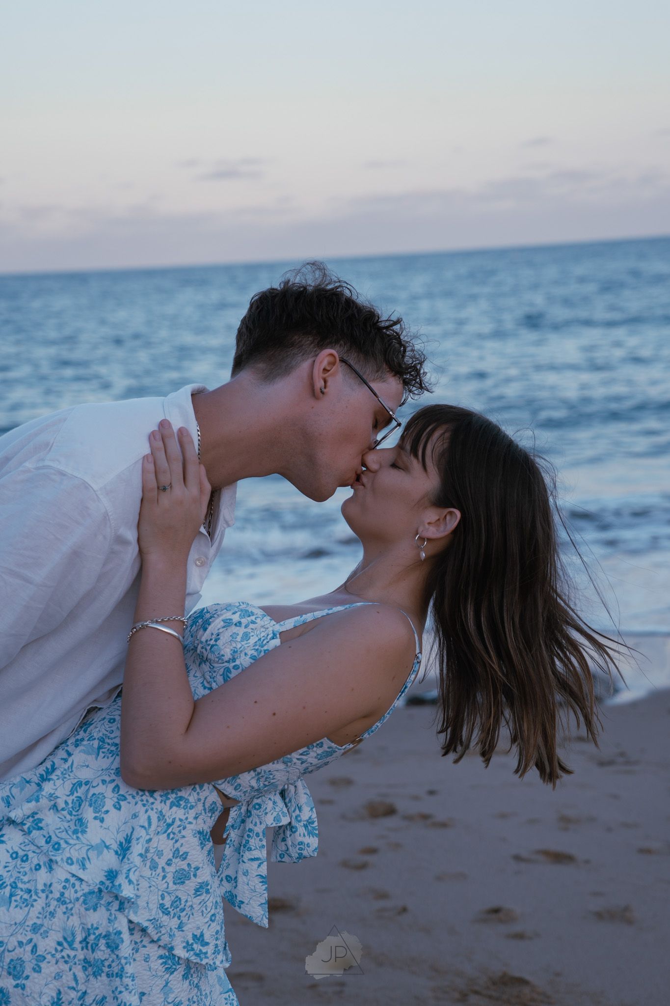 Romantic couple shares intimate moments on a beach at sunset with ocean waves in the background.
