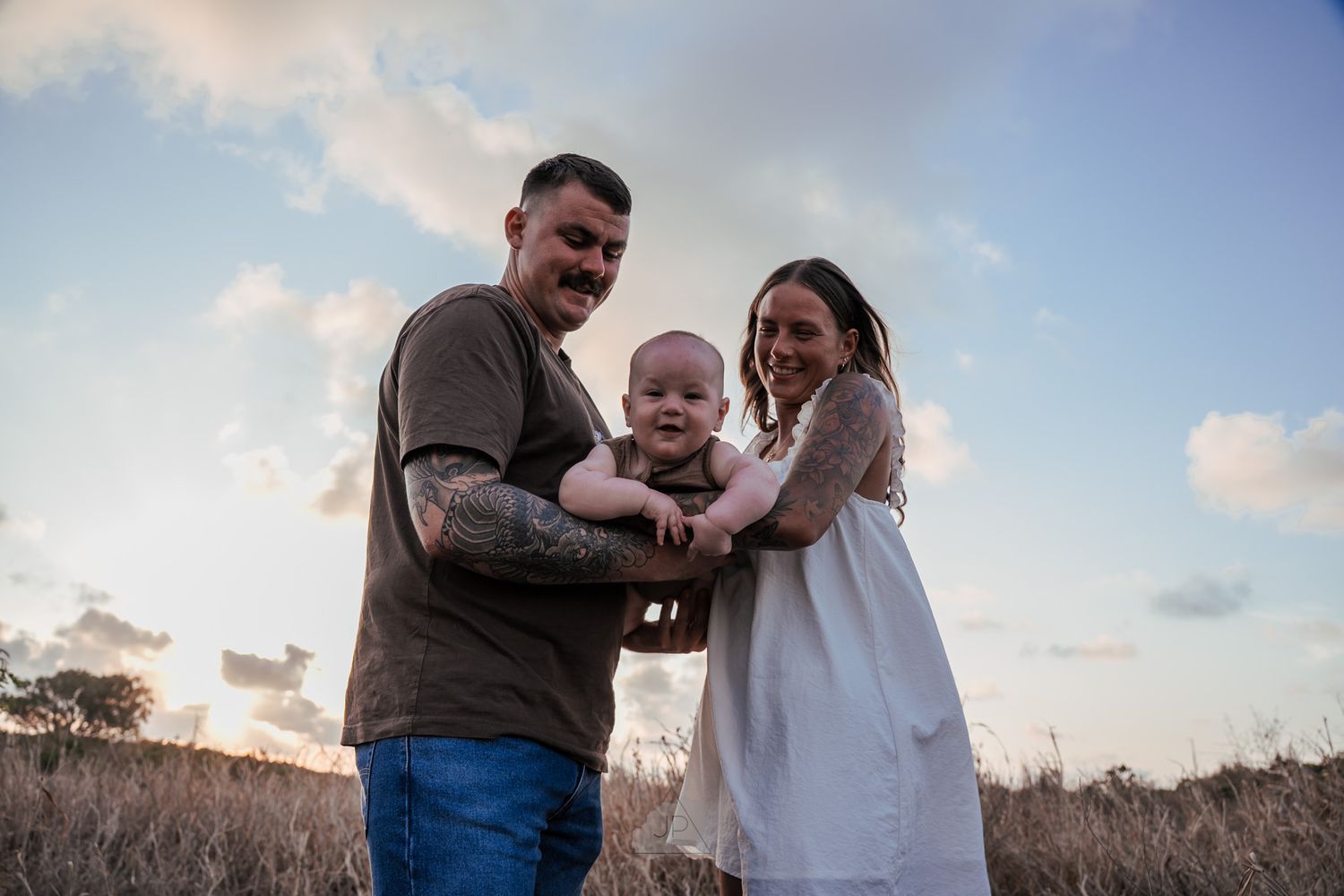 A couple shares joyful moments together during a golden hour photoshoot in an outdoor field setting.