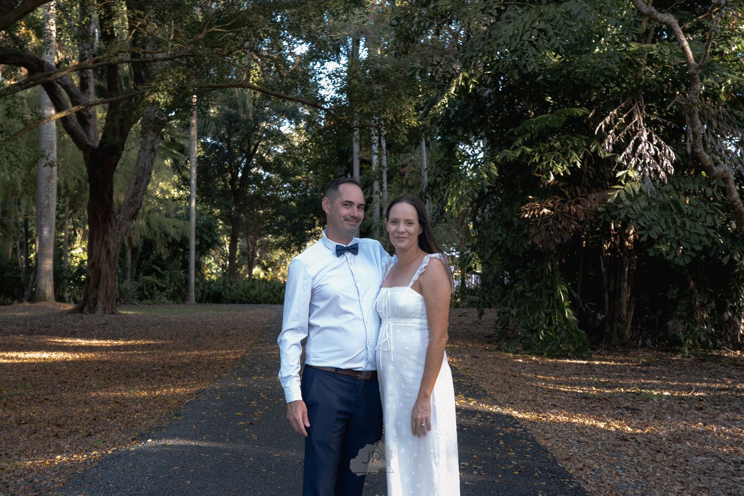 A couple poses for romantic outdoor photos in a wooded park setting during golden hour.