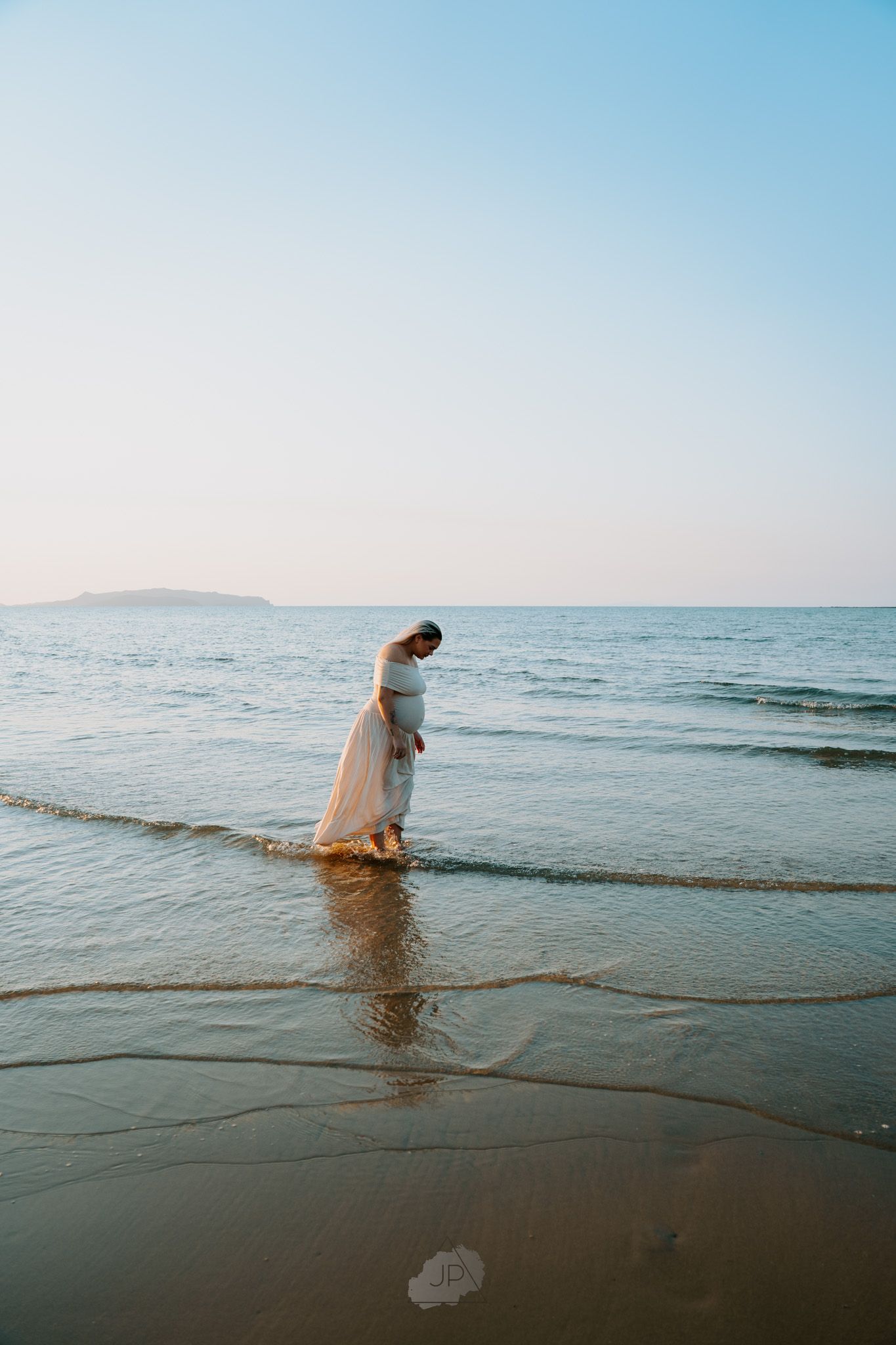A figure in white clothing wades into the calm ocean waters during a serene beachside photoshoot.
