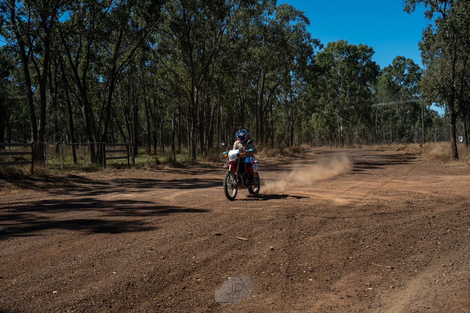 Motorcyclist riding through a winding dirt trail in Australian bushland with eucalyptus trees lining the path.