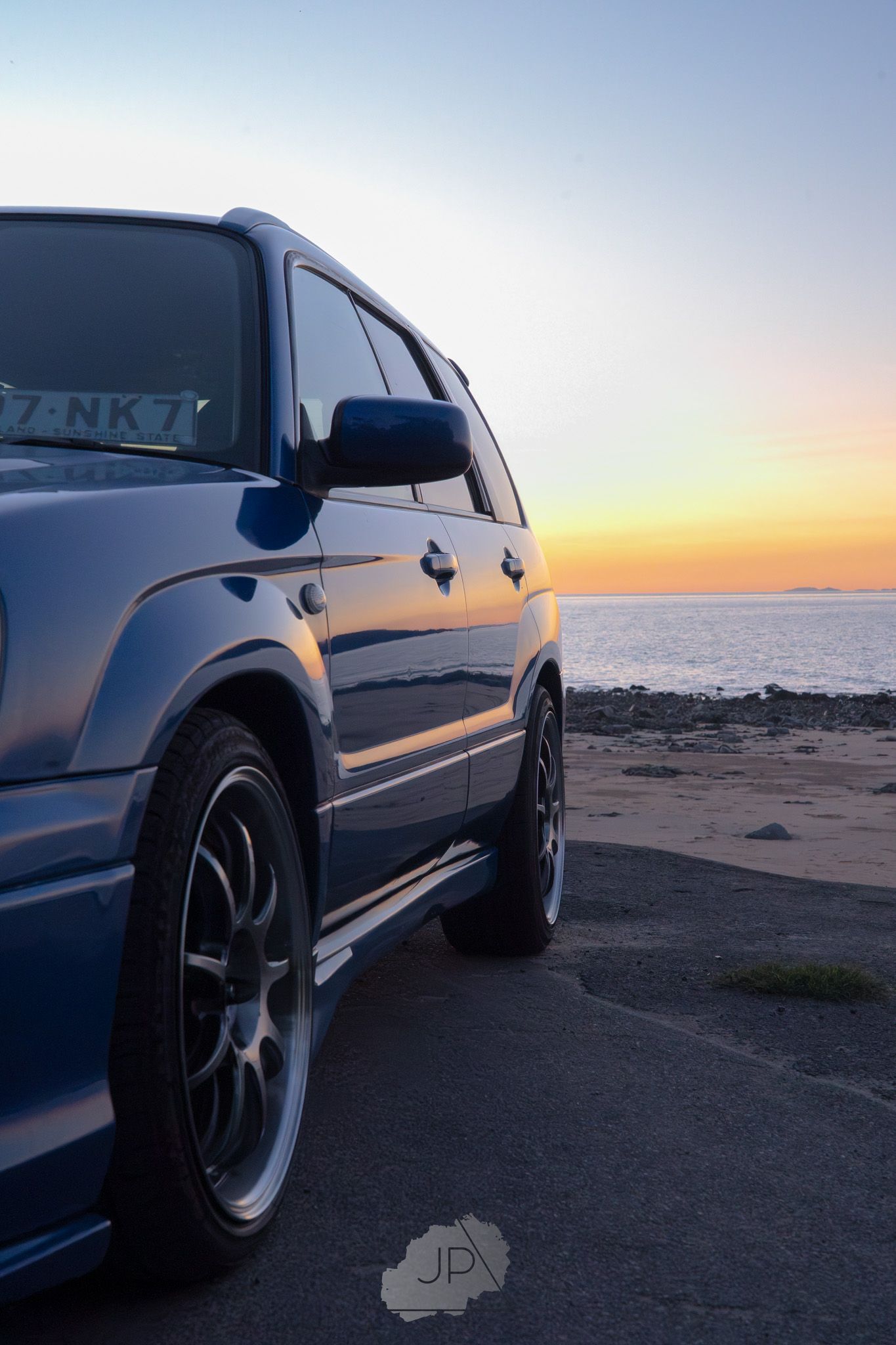 Silver SUV parked at the beach during a stunning orange sunset over the ocean horizon.
