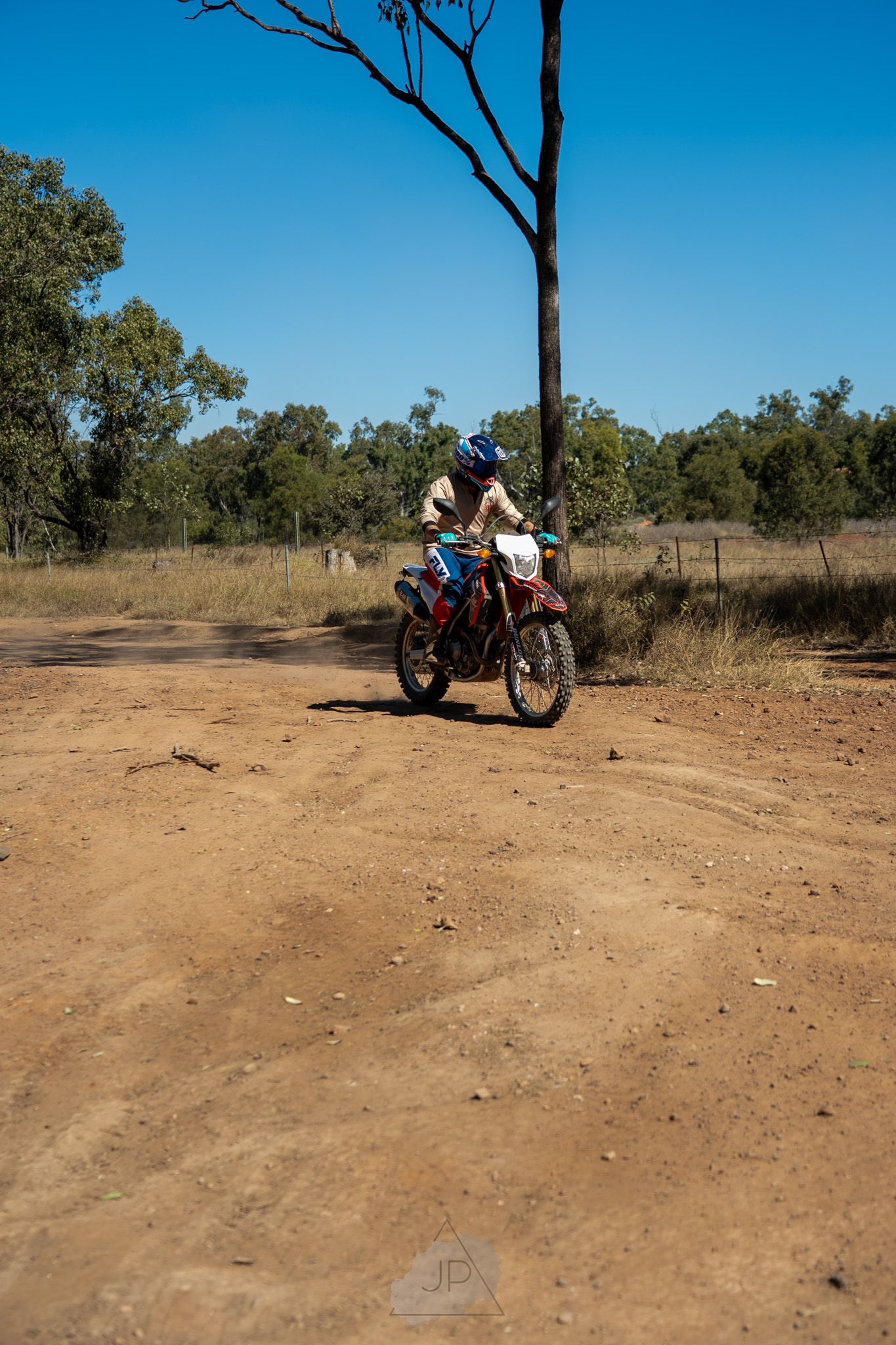 A motorcycle parked on a dirt path surrounded by Australian bush vegetation and gum trees.