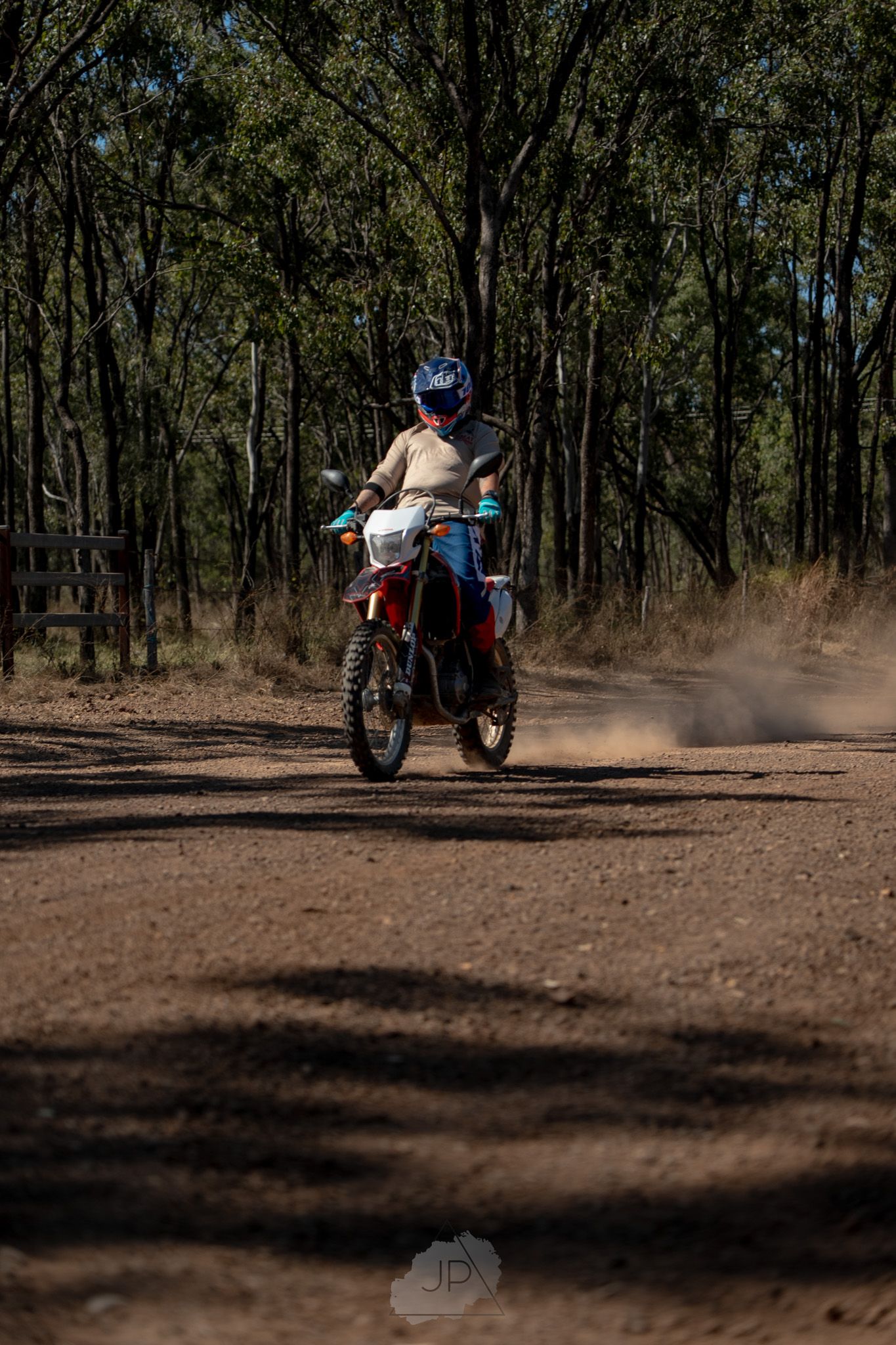 A sequence of motorcycle riders kicking up dust while riding through a wooded forest trail in dramatic lighting.