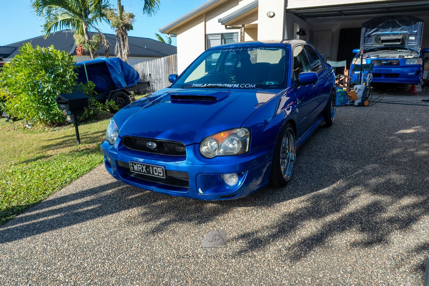 A line of modified blue Subaru WRX cars parked on a sunny day showing their sleek front-end designs and custom features.