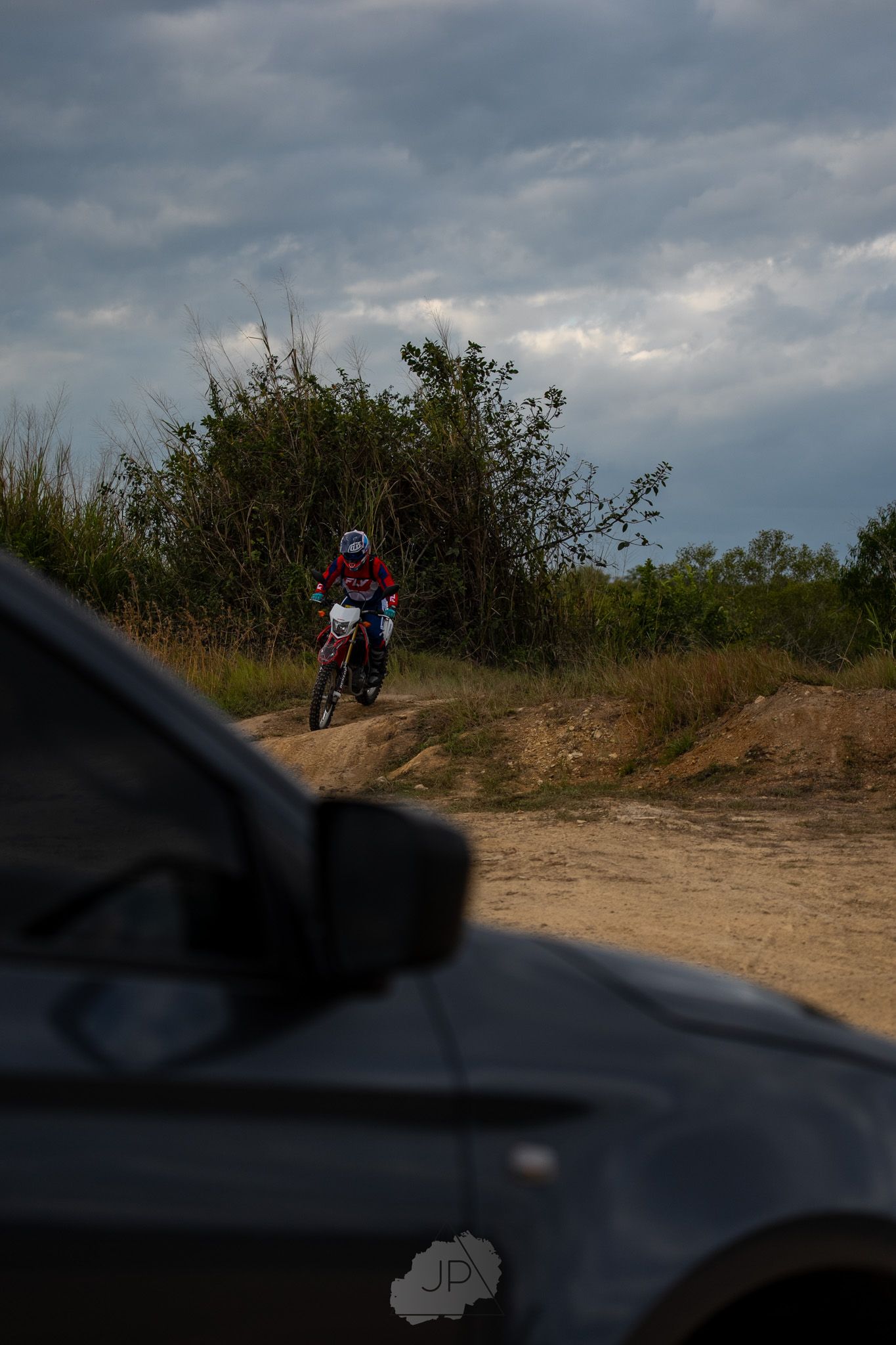 Dirt bike rider silhouetted against cloudy sky on off-road terrain at dusk.