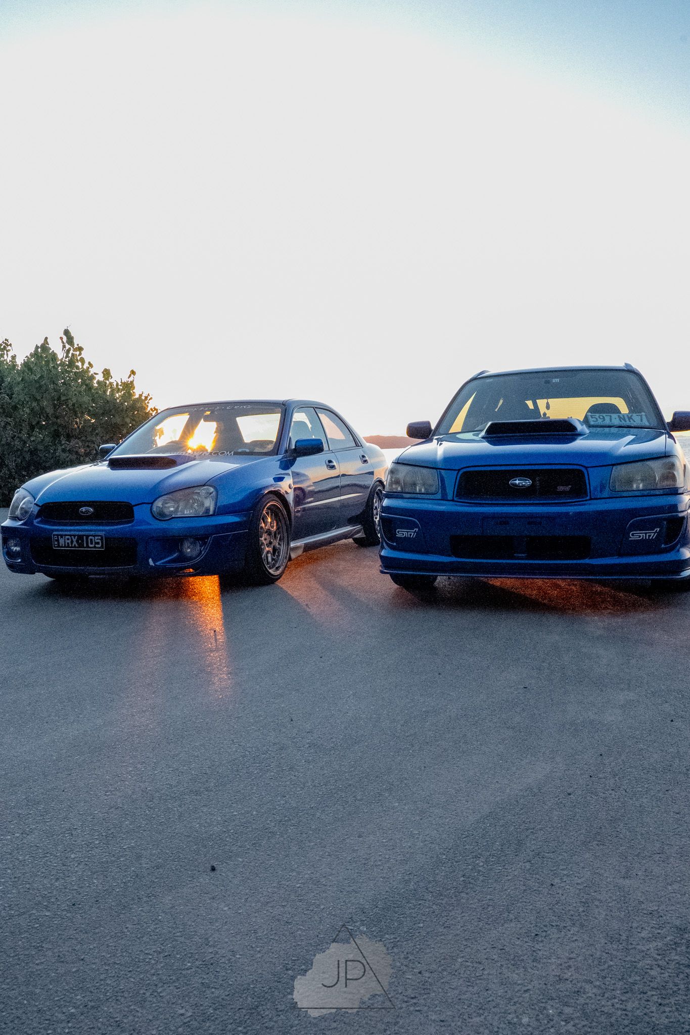 A row of blue Subaru WRX sports cars lined up at sunset against a darkening sky.