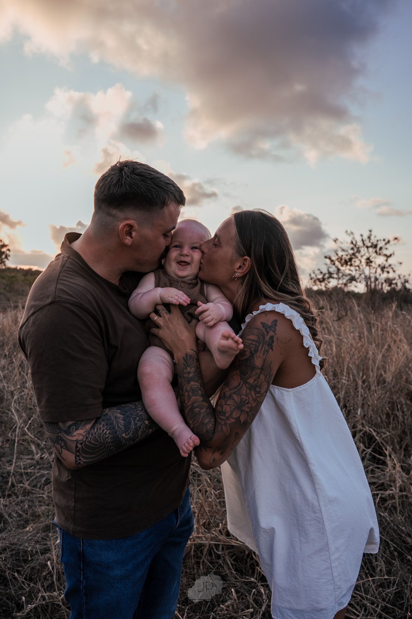 A family embraces and shares kisses with their baby during a golden hour portrait session in nature.