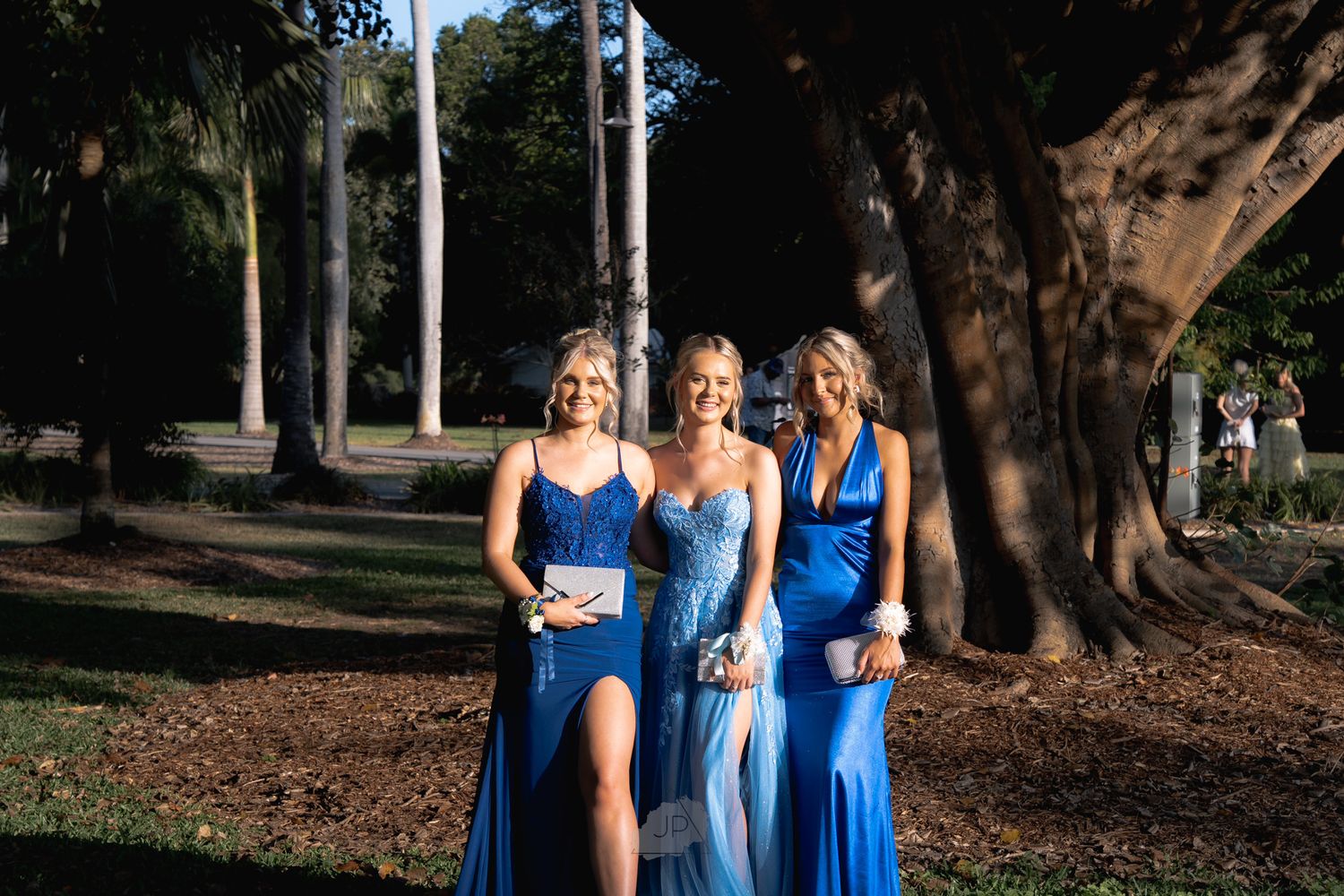 A group of people wearing coordinated blue dresses pose together in a wooded outdoor setting.