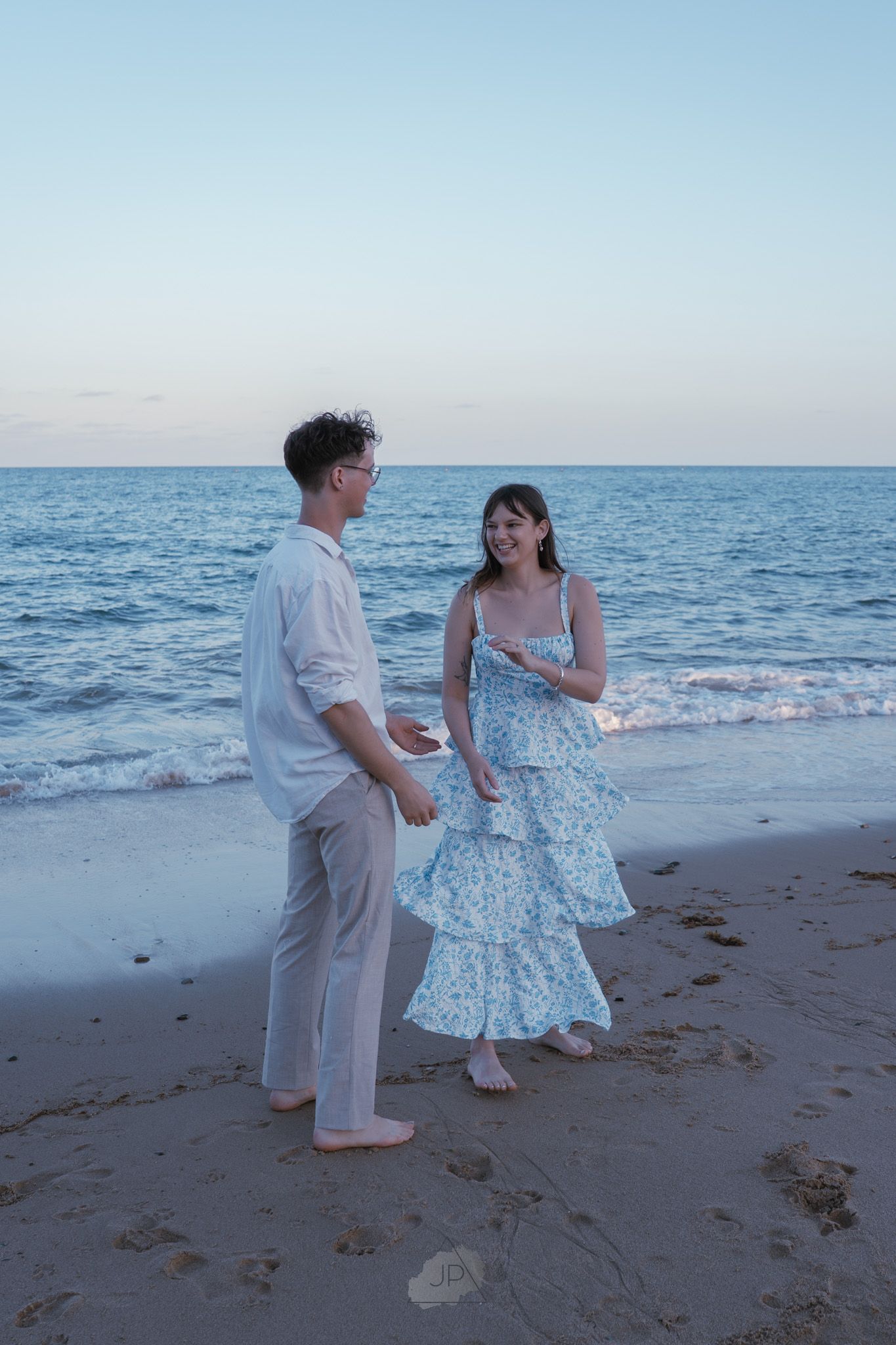 A couple dances together on a beach at sunset, with the ocean waves visible in the background.