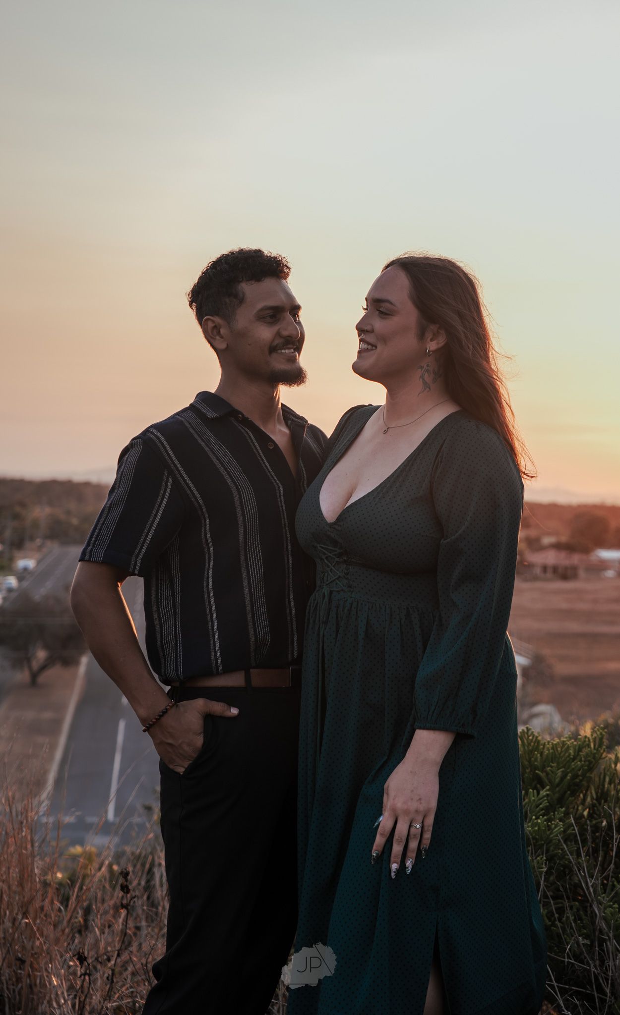 A couple shares a romantic moment together at sunset on a hilltop overlooking a city.