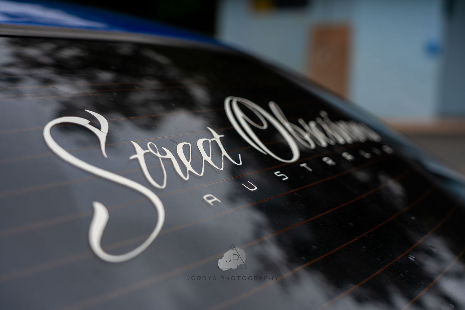 Stylish white Street Outlaws cursive logo decal displayed on a glossy black car surface.