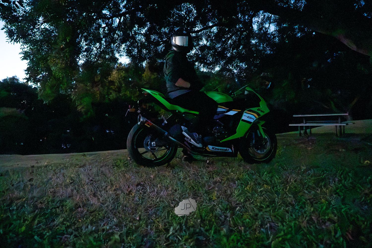 Two images of a black motorcycle parked on grass, with trees and natural scenery in the background during daytime.