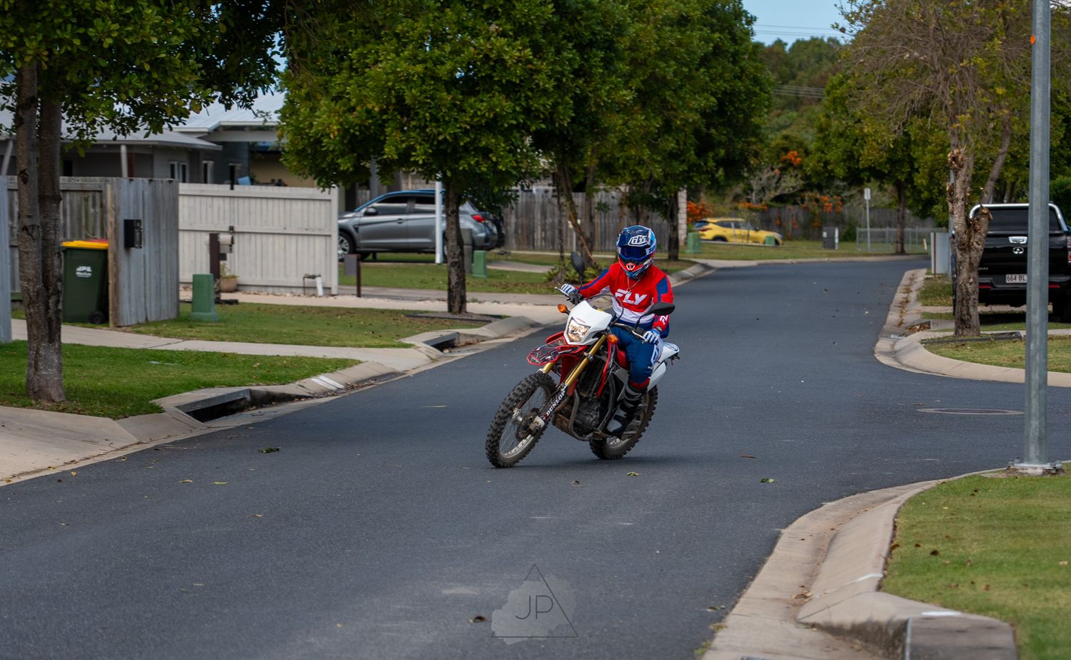 Red motorcycle parked on a curved residential street with green trees and houses in the background.