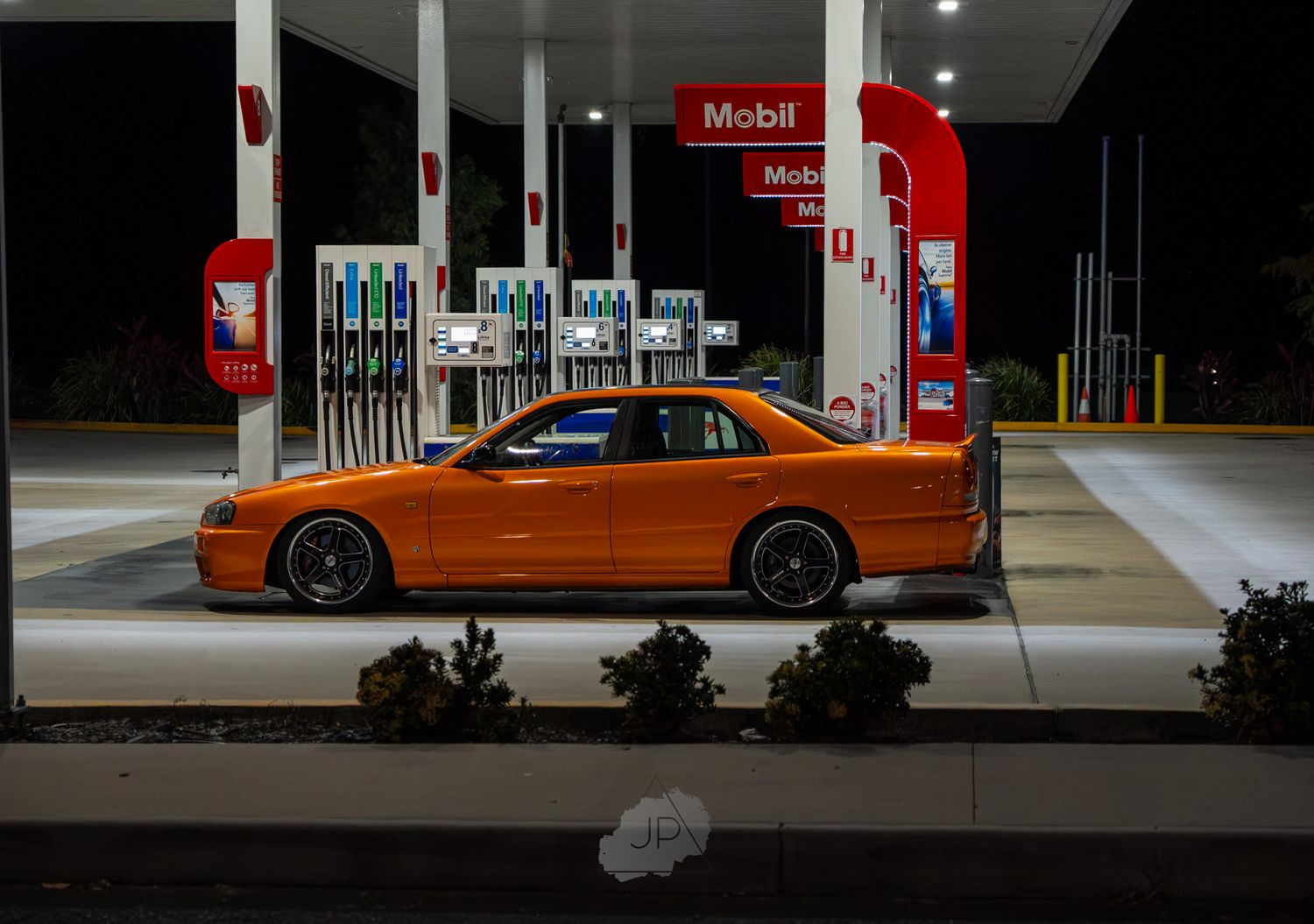 Orange sports car parked at night under bright lights at a Mobil gas station.