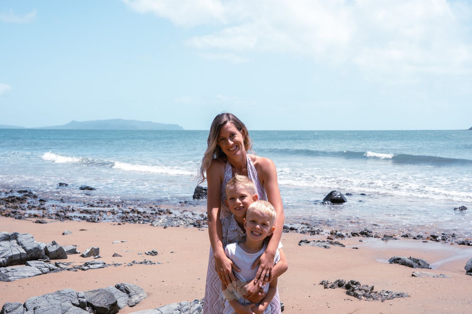 A group of people enjoying a sunny day at a scenic beach with waves crashing on the rocky shoreline.