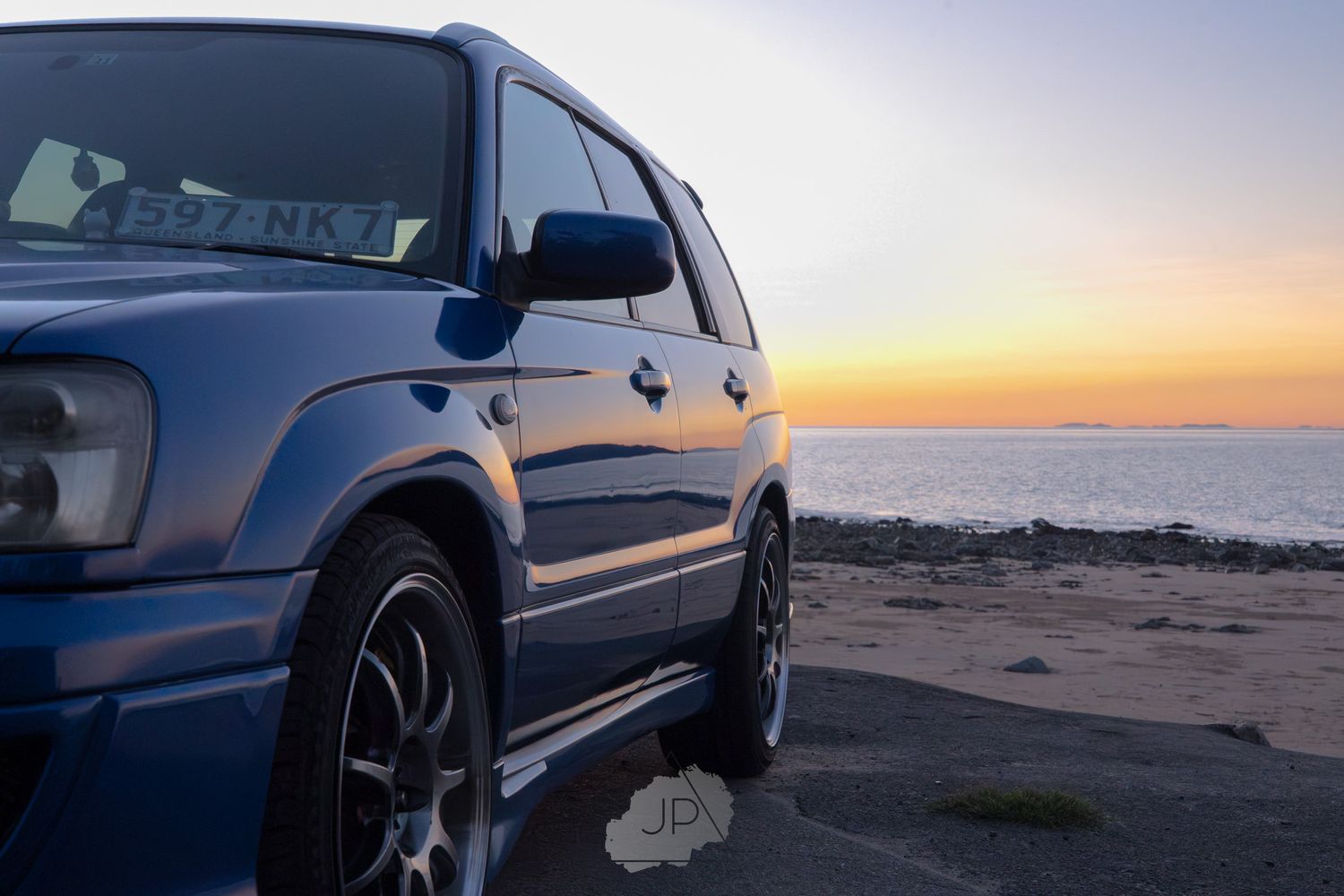 A row of silver Mercedes SUVs parked along a desert beach at sunset with their headlights illuminating the sand.