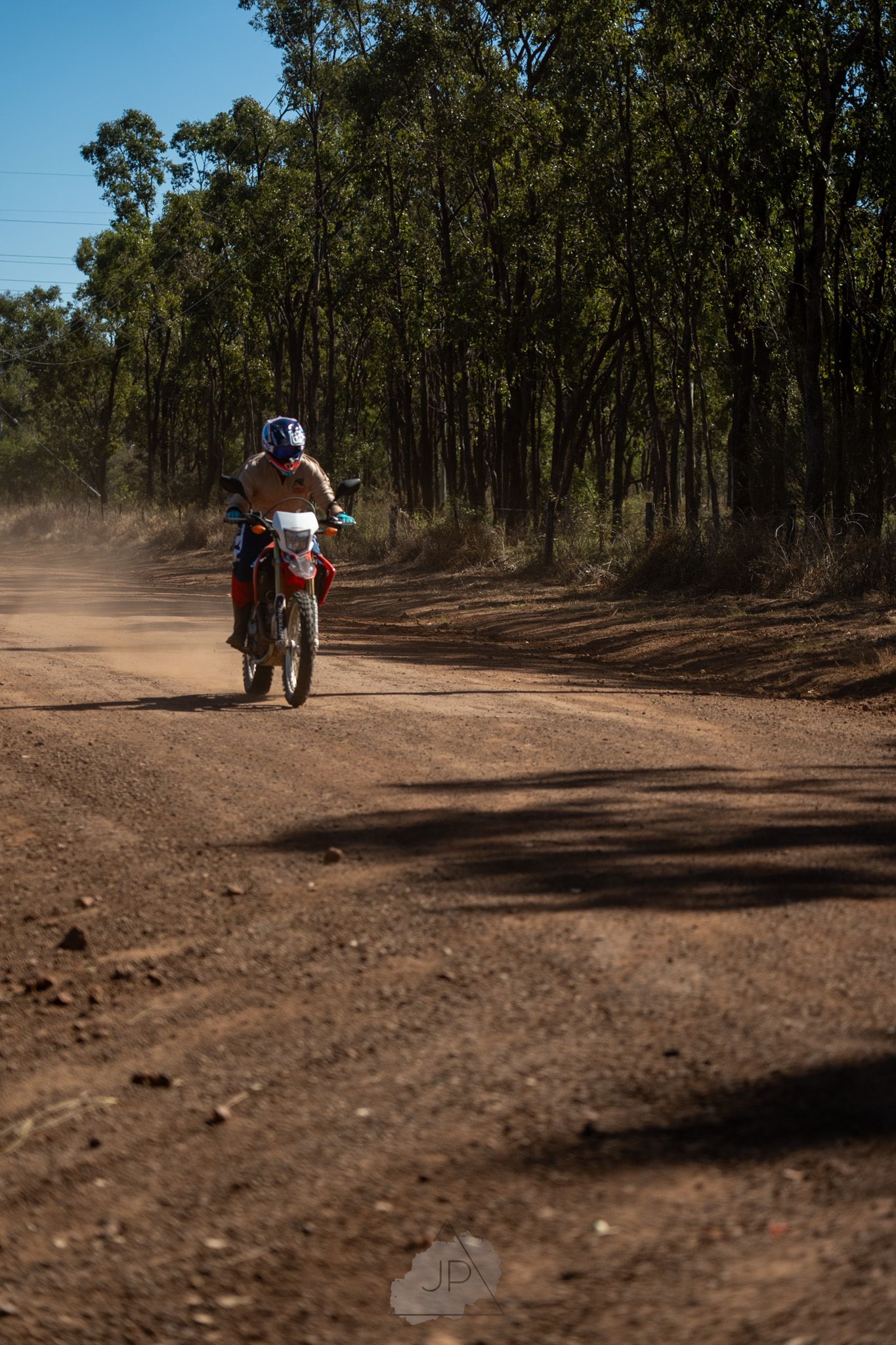A dirt bike rider kicks up dust while riding through a eucalyptus forest on a dusty trail in Australia.
