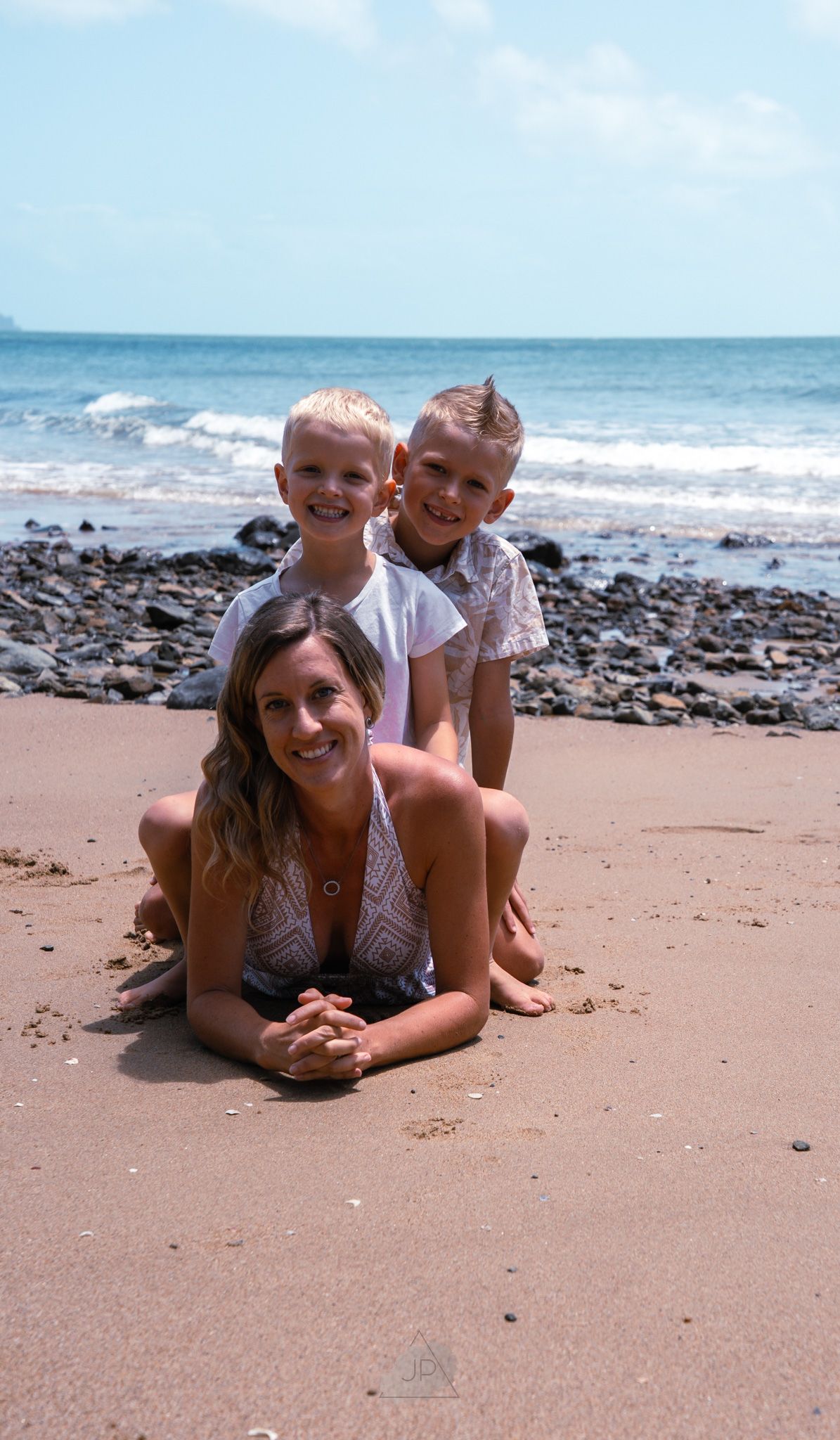 Two people laying on a sandy beach with ocean waves and rocky shoreline in the background.